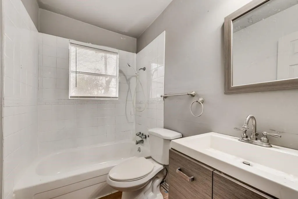 White tiled shower/tub combination with a window, modern vanity with wood-finish cabinetry, and a framed mirror