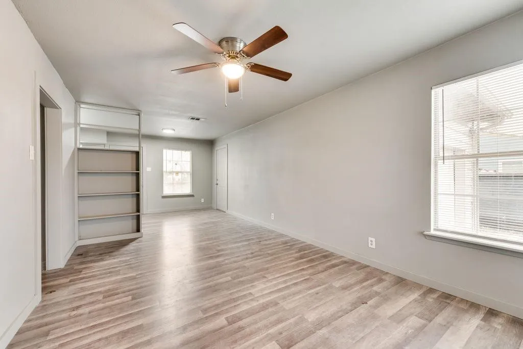 Wood-finish flooring, built-in shelving, ceiling fan with integrated lighting, and multiple windows