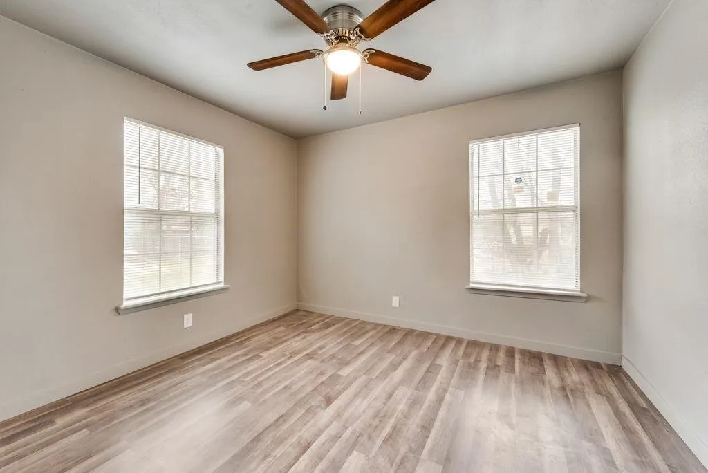 Wood-finish flooring, two windows, and a ceiling fan with integrated lighting