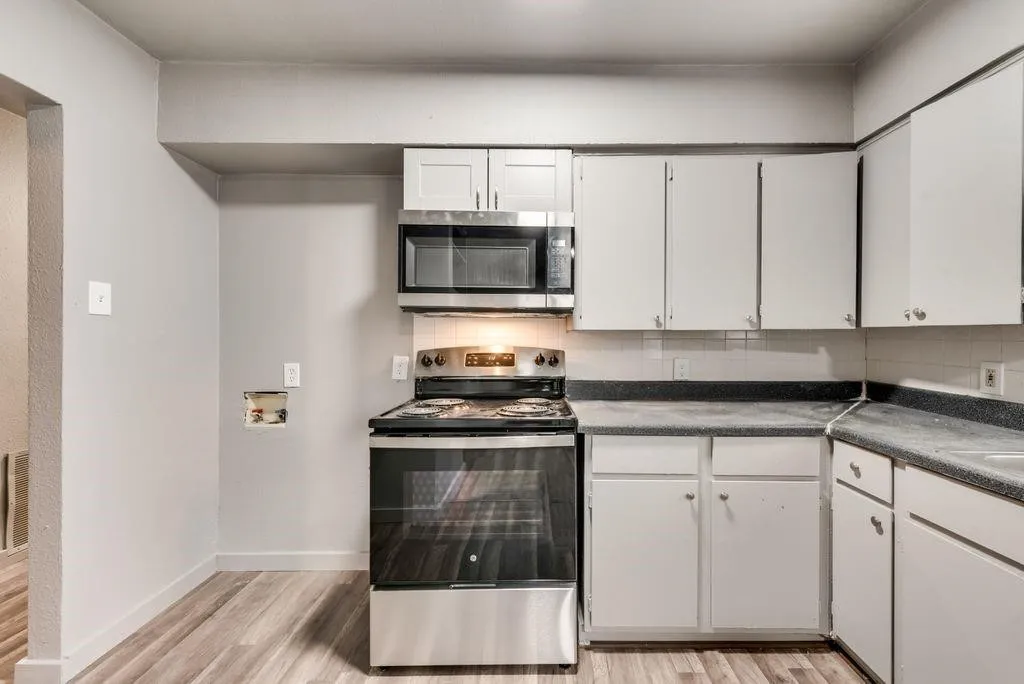 Kitchen featuring wood-finish flooring, white cabinetry, a stainless steel oven/range, a built-in microwave, and dark countertops