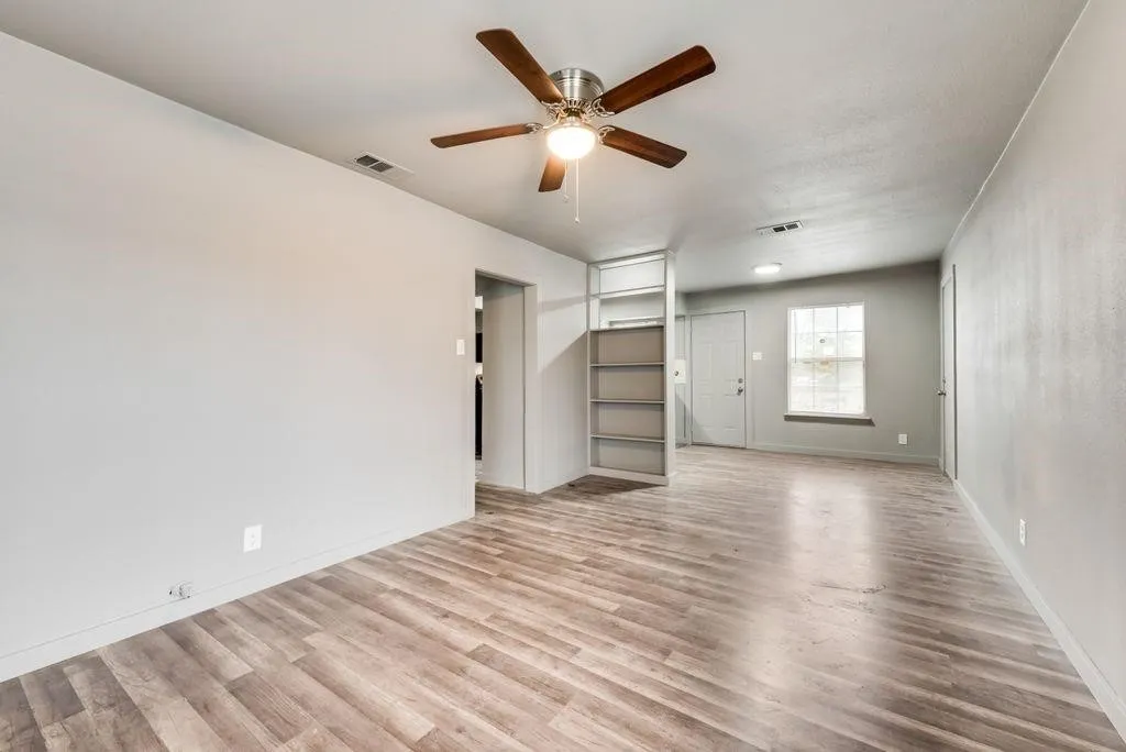 Spacious interior with wood-finish flooring, a ceiling fan, and built-in shelving