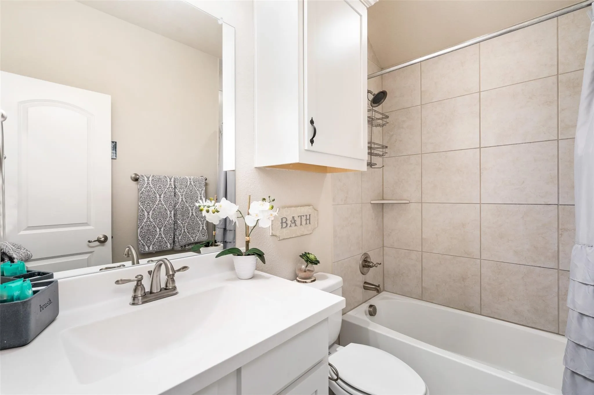 Vanity with integrated sink, white cabinetry with dark hardware, full-width mirror, tile shower surround, and built-in tub