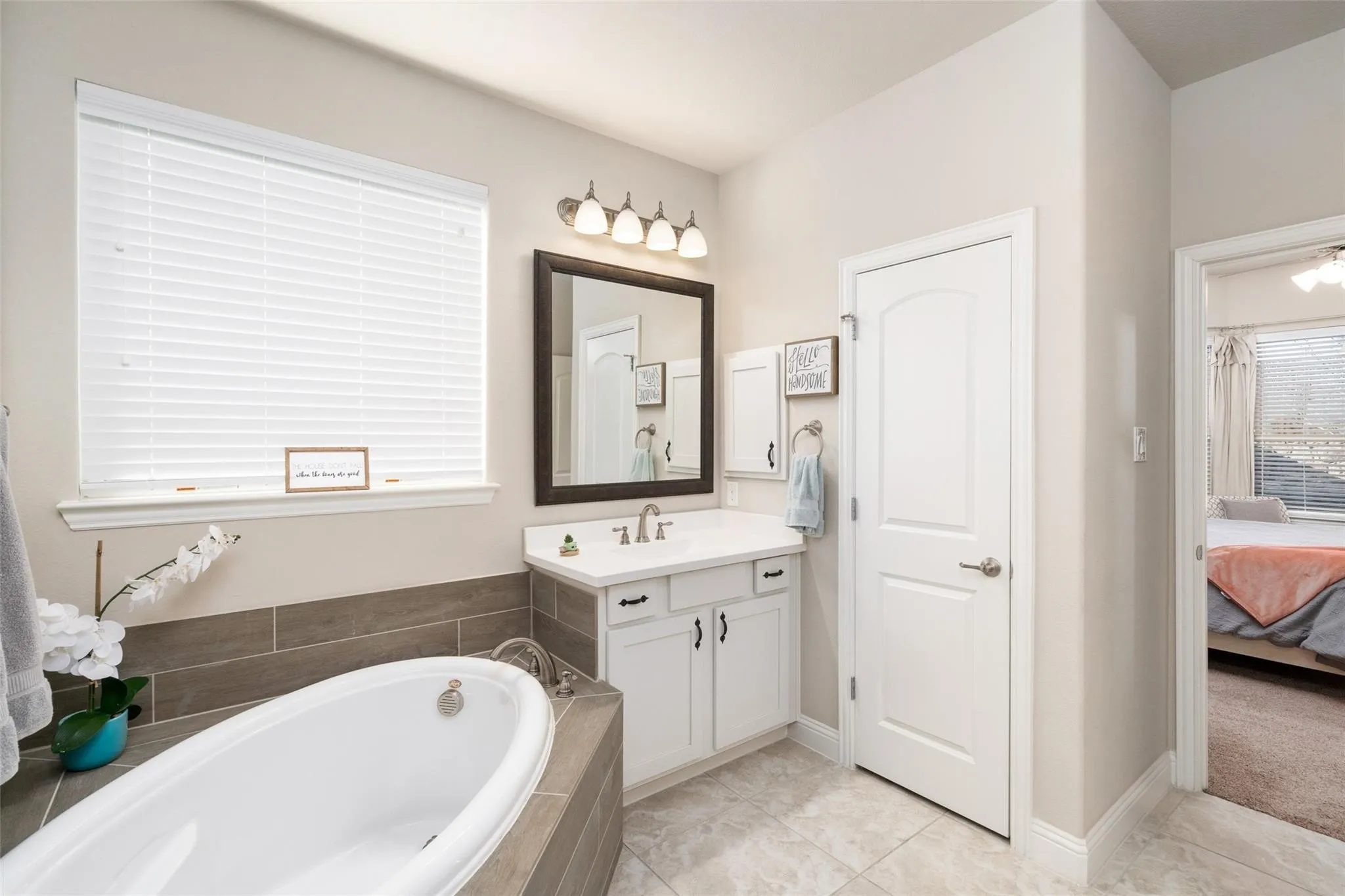 Soaking tub with tile surround, single vanity with integrated sink, rectangular mirror, and sconce lighting