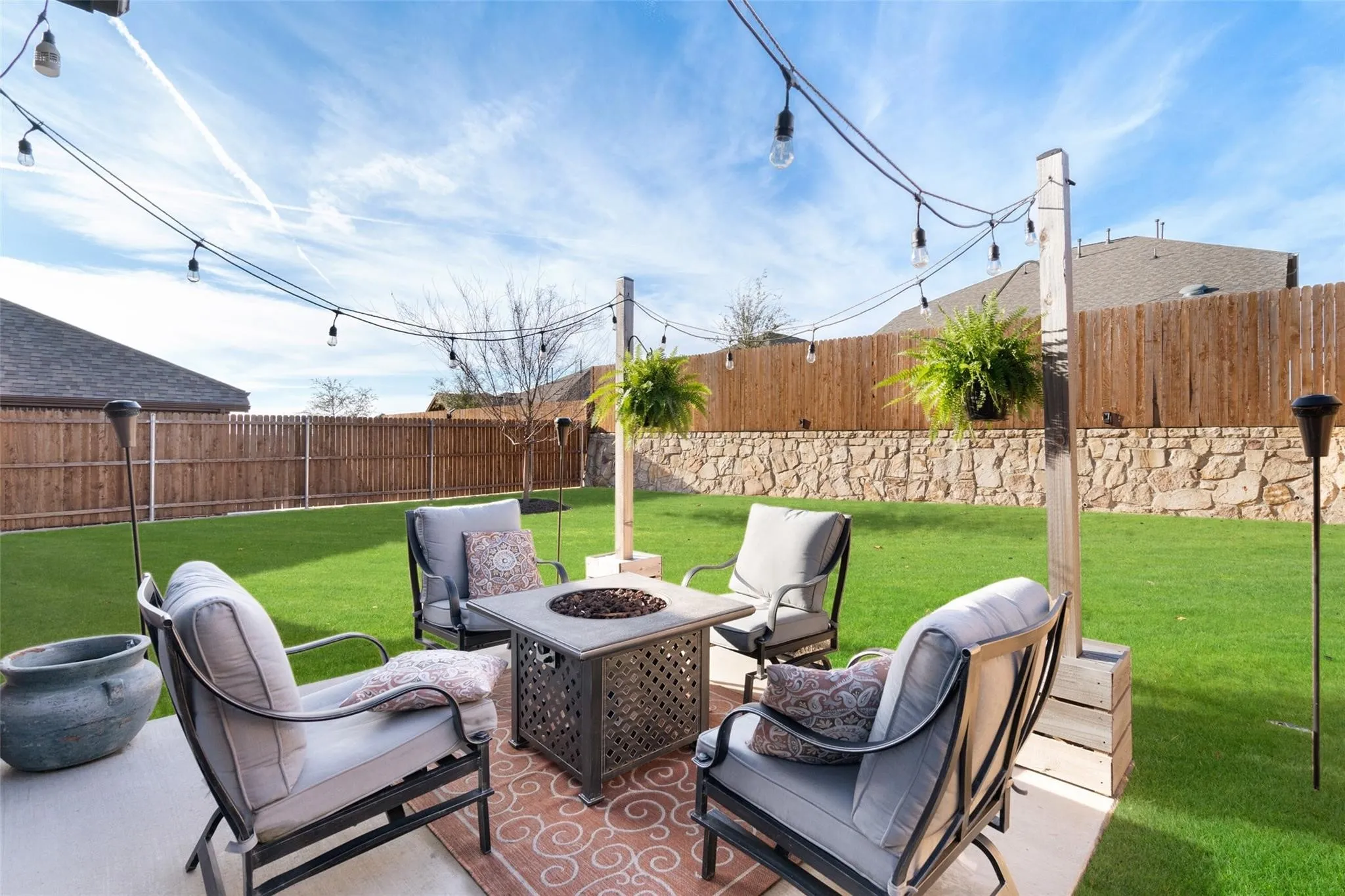 Expansive backyard featuring a manicured lawn, wood privacy fencing, stone wall accent, string lighting, and a paved patio area