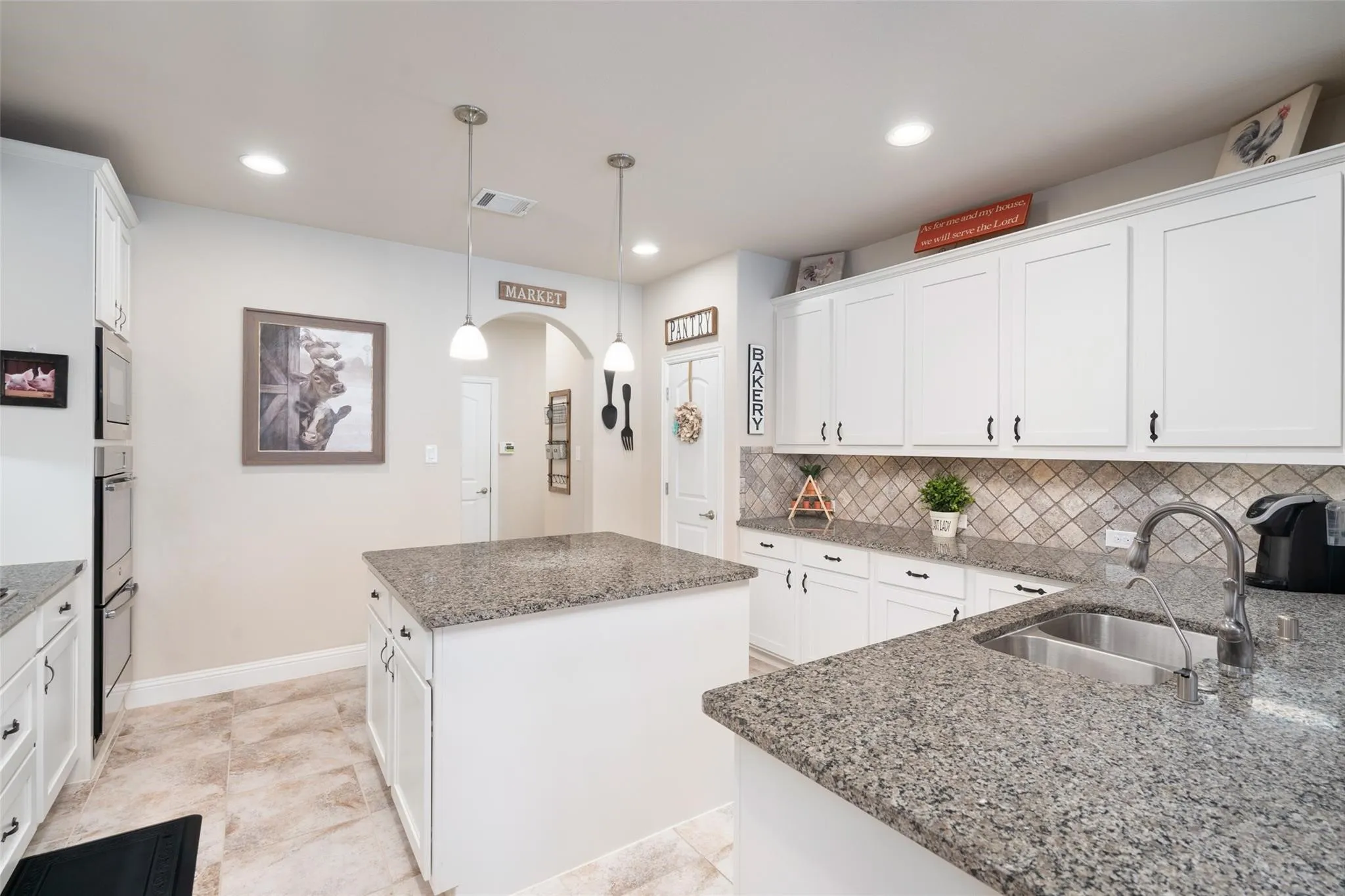Kitchen featuring a central island, double oven, white cabinetry, tile backsplash, and stone countertops