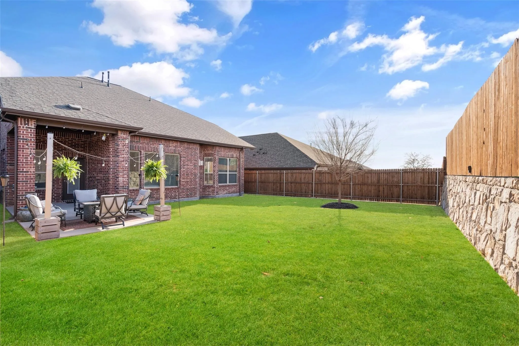 Expansive backyard featuring a covered patio with brick columns, a stone and wood privacy fence, and a manicured lawn