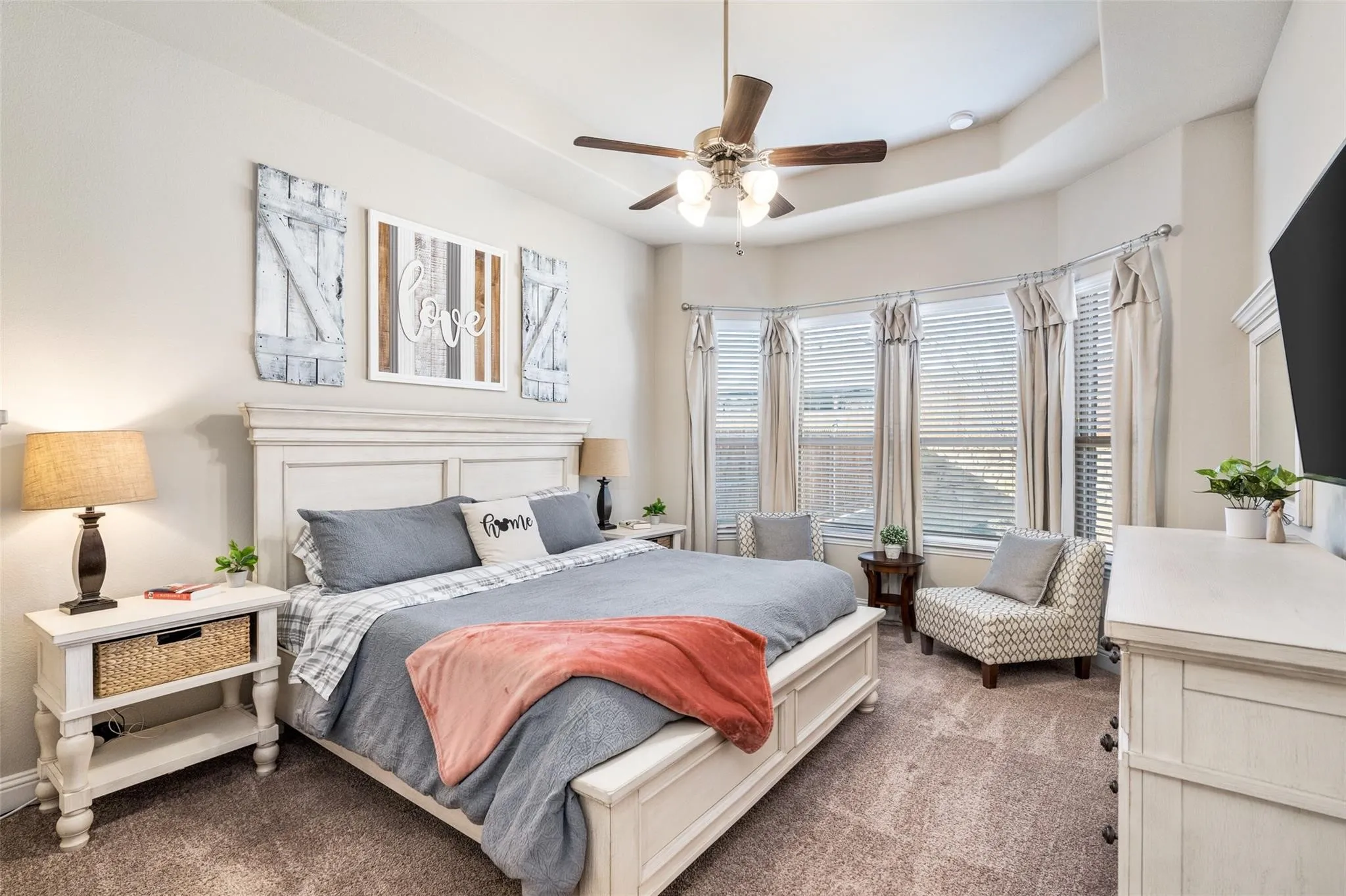 Tray ceiling with a ceiling fan, bay window with blinds and drapes, and carpeted flooring