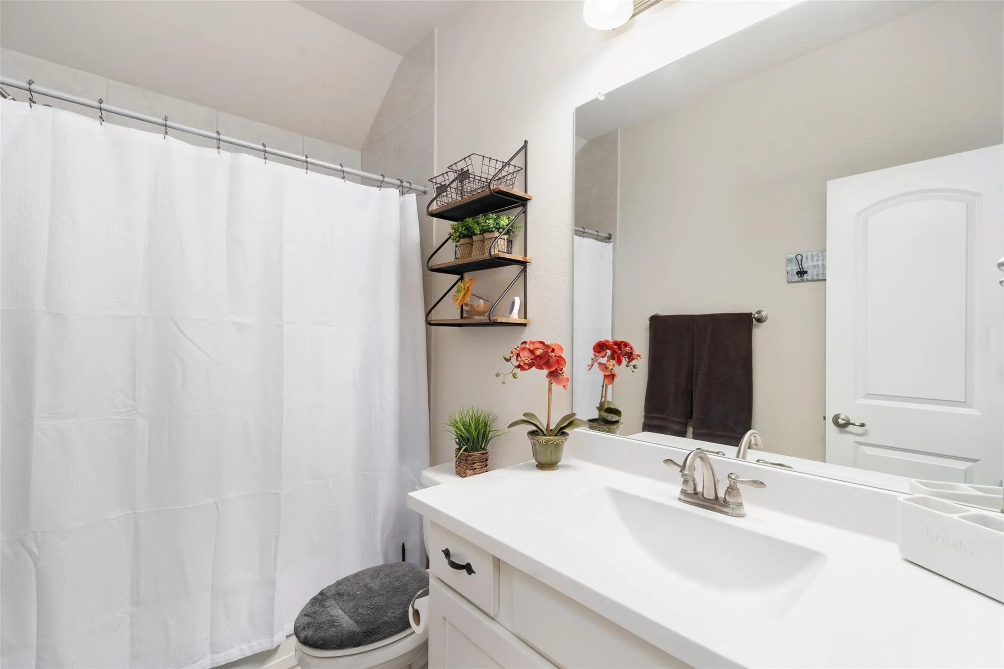 White vanity with an integrated sink, brushed nickel faucet, wall-mounted mirror, and a shower with a privacy curtain