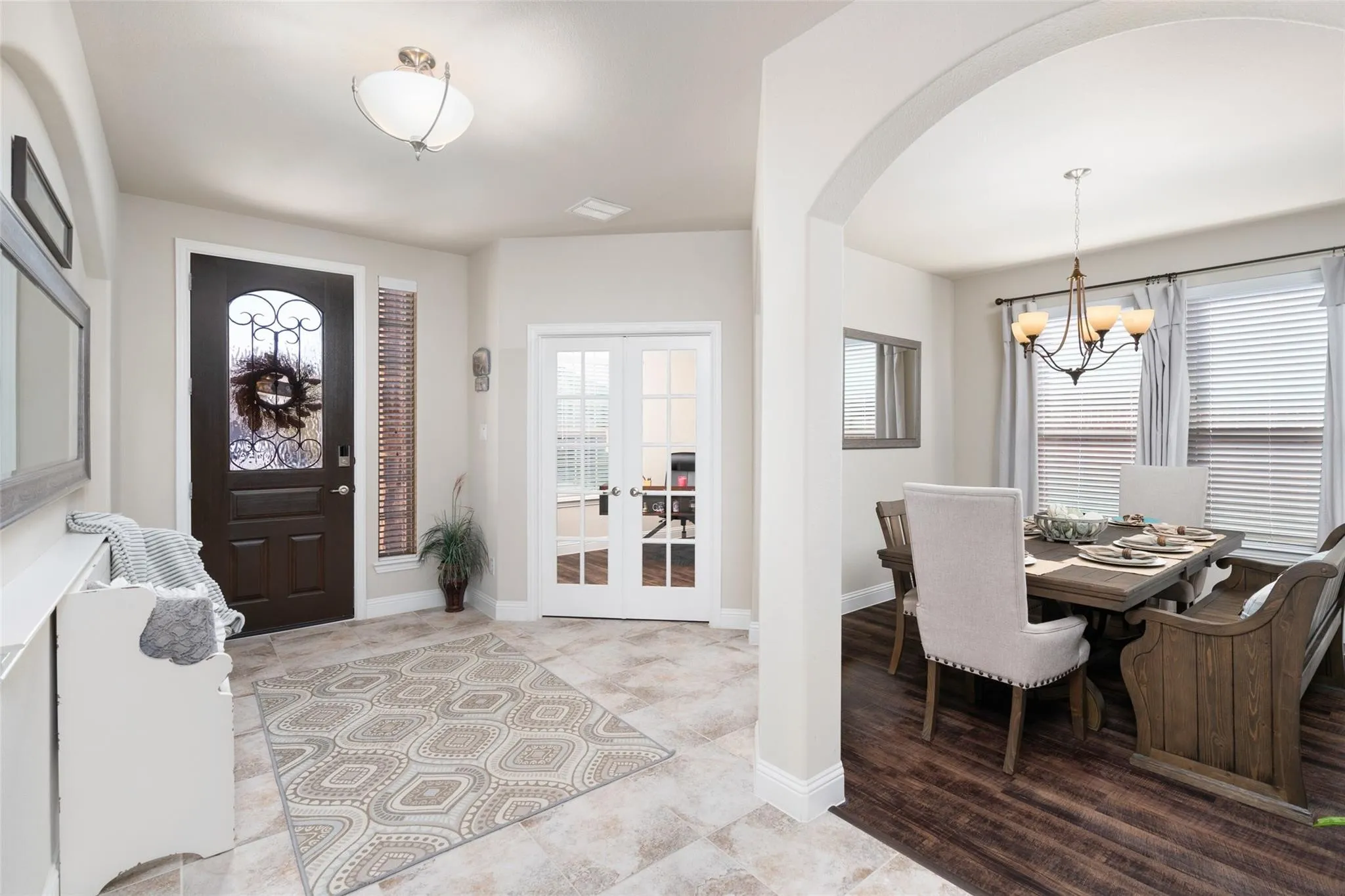 Arched entryway, tile flooring, dark wood entry door with ornate glass, French doors, and a dining area with wood-finish flooring