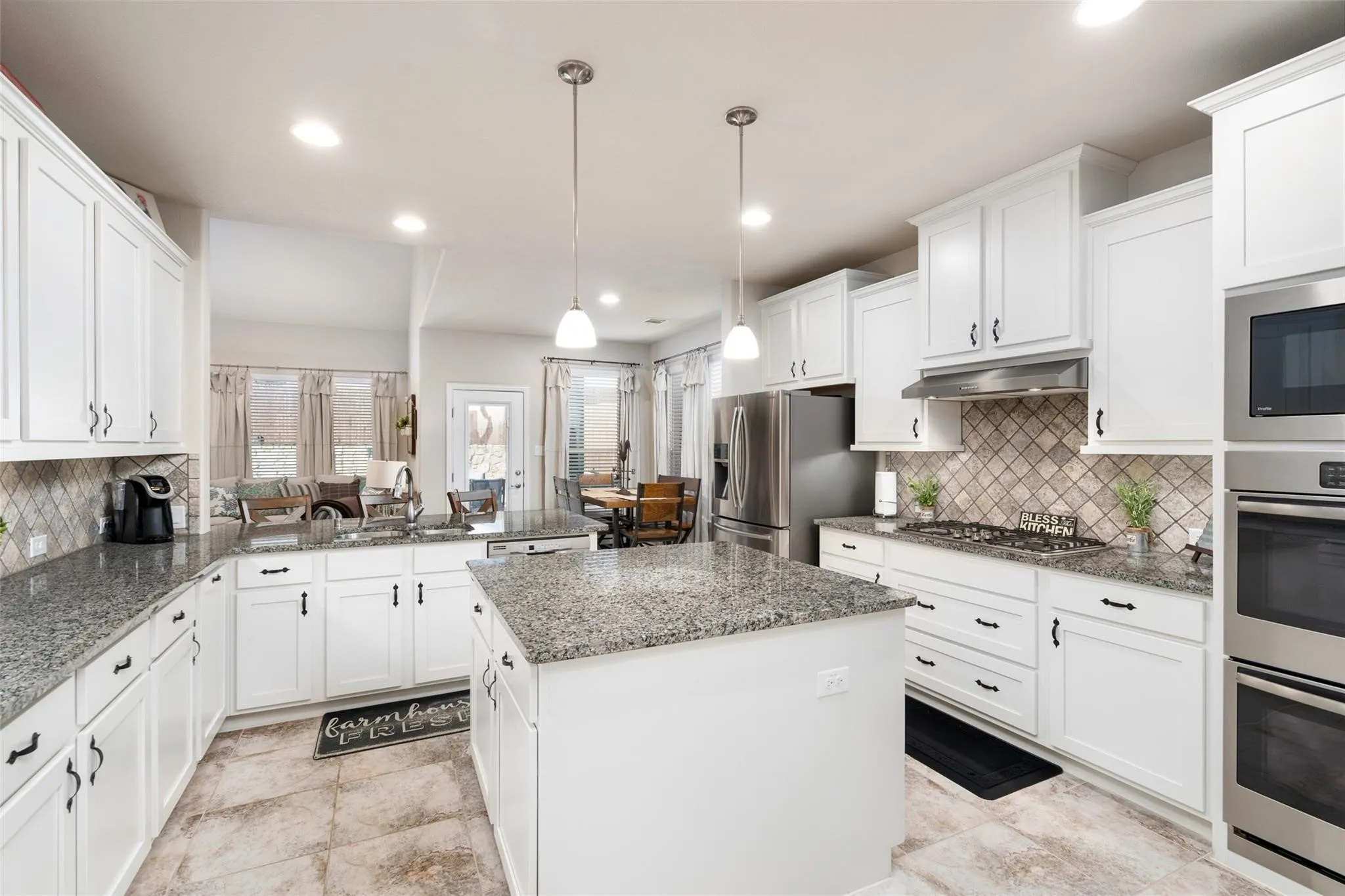 White cabinetry with black hardware, granite countertops, stainless steel appliances, tile flooring, and a decorative tile backsplash