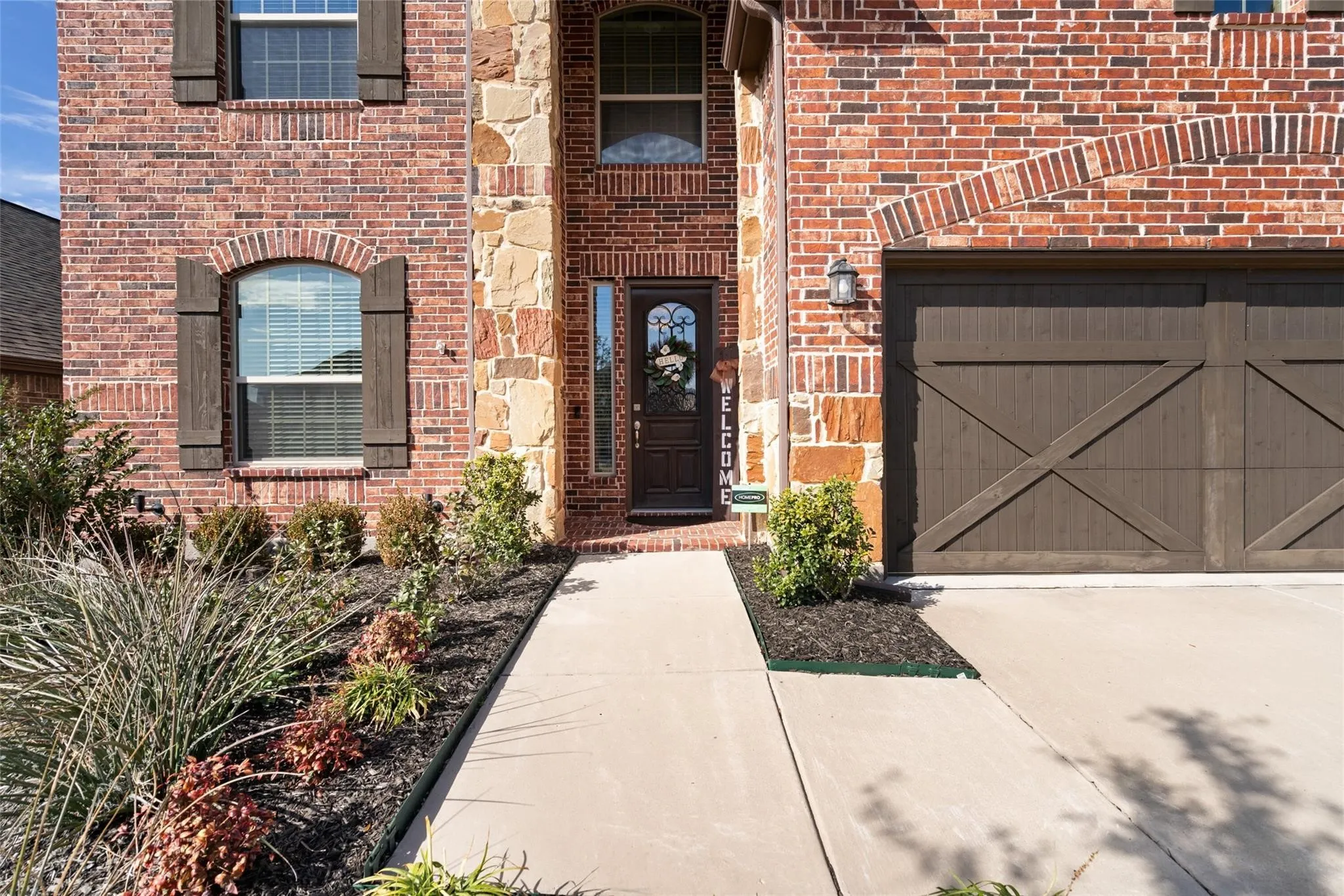 Brick and stone exterior featuring an arched entryway, decorative wooden garage door, and established landscaping