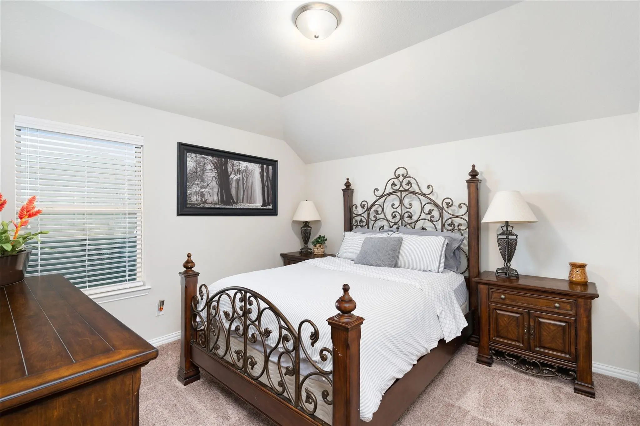 Vaulted ceiling, window with blinds, and neutral-toned carpeting
