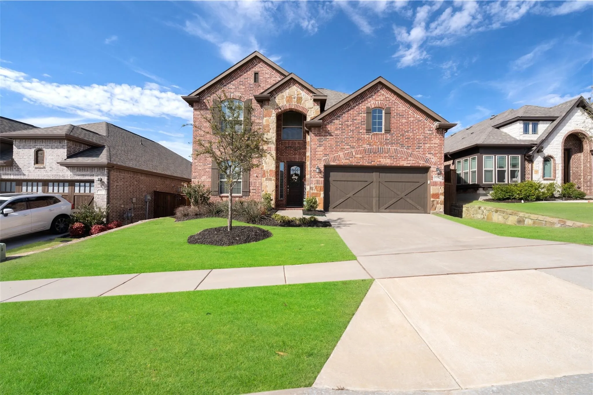 Brick exterior with stone accents, arched entry, two-car garage with cross-brace doors, concrete driveway, and a front lawn