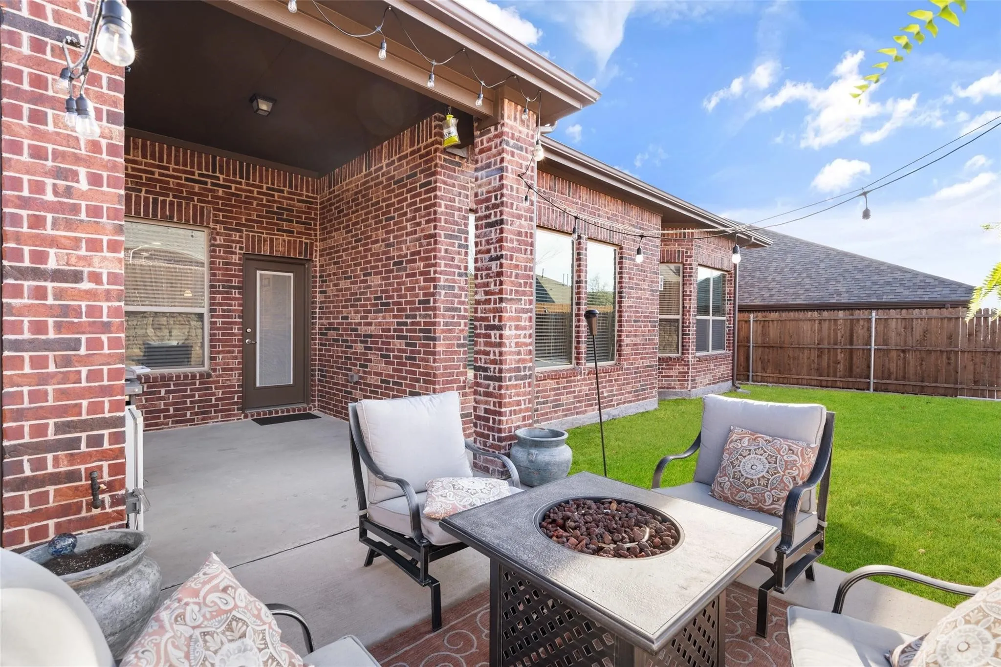 Covered concrete patio featuring brick columns, exterior brick siding, and multiple windows