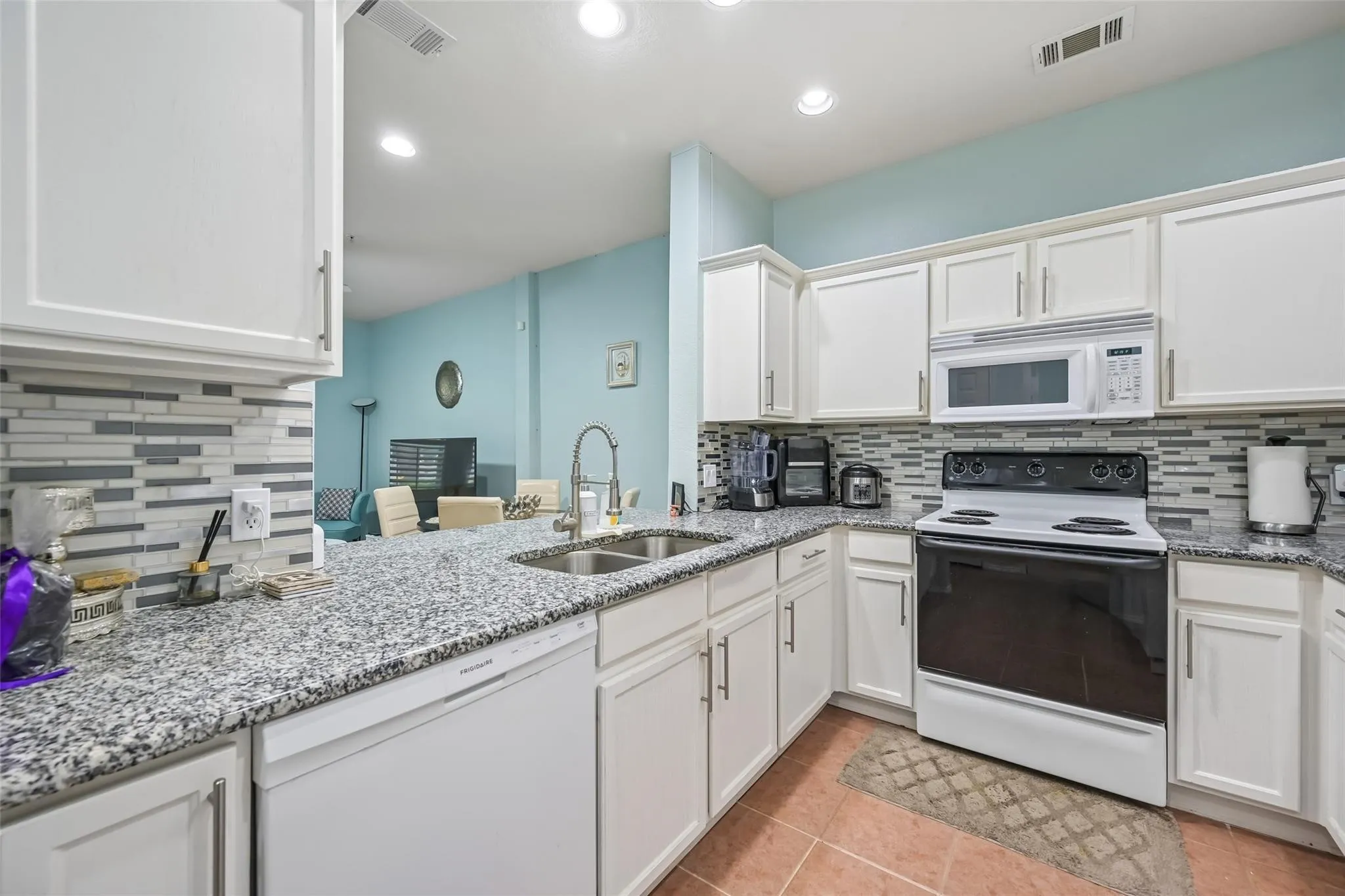 Kitchen featuring white cabinetry, granite countertops, tile backsplash, built-in microwave, and a double basin sink