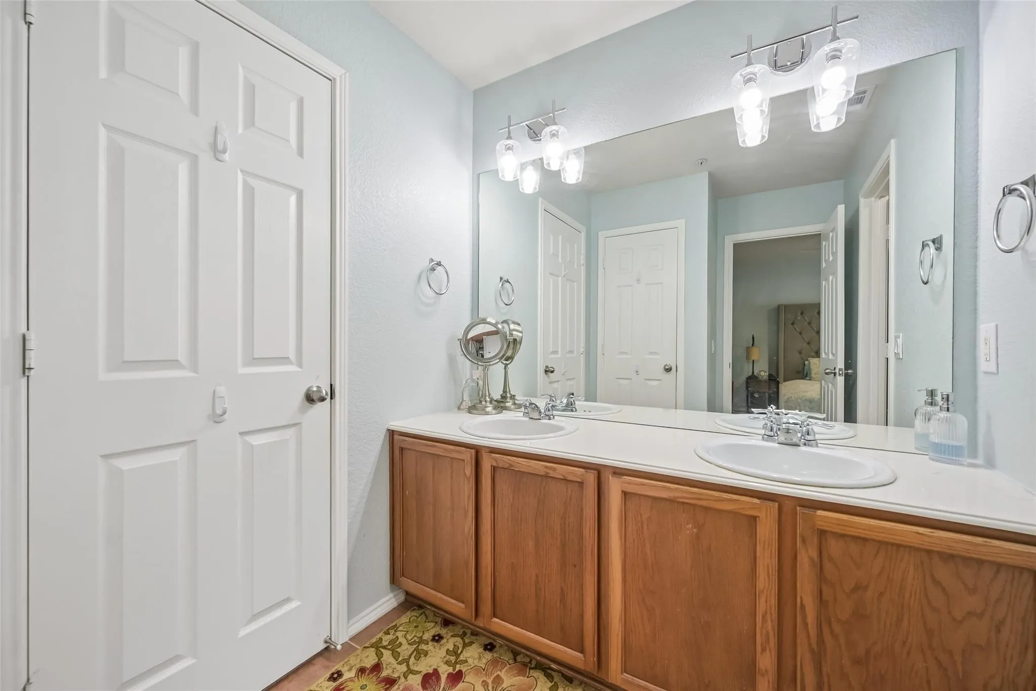 Dual vanity with integrated sinks, wood-finish cabinetry, and a full-width mirror with overhead lighting