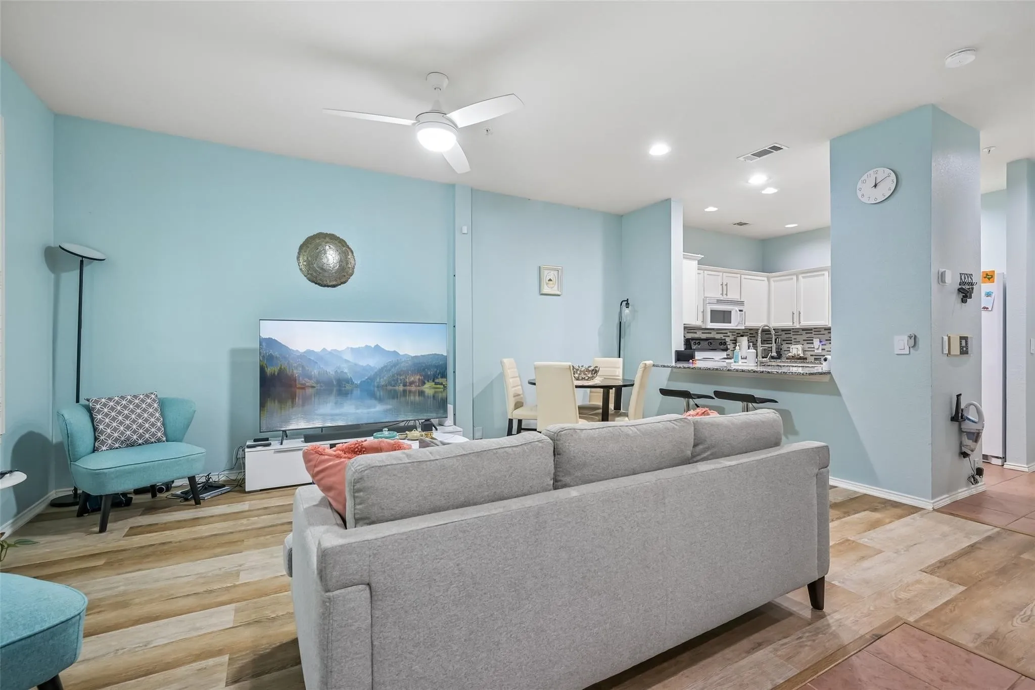 Open-concept living area featuring wood-finish flooring, recessed lighting, a ceiling fan, and a kitchen with white cabinetry and a breakfast bar