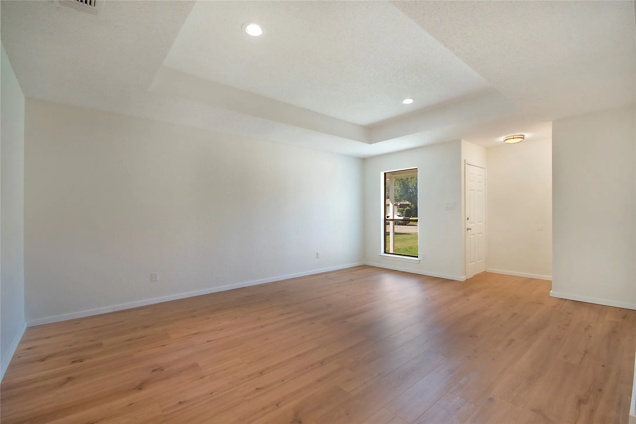 Recessed lighting, wood-finish flooring, tray ceiling, single window, and a white entry door
