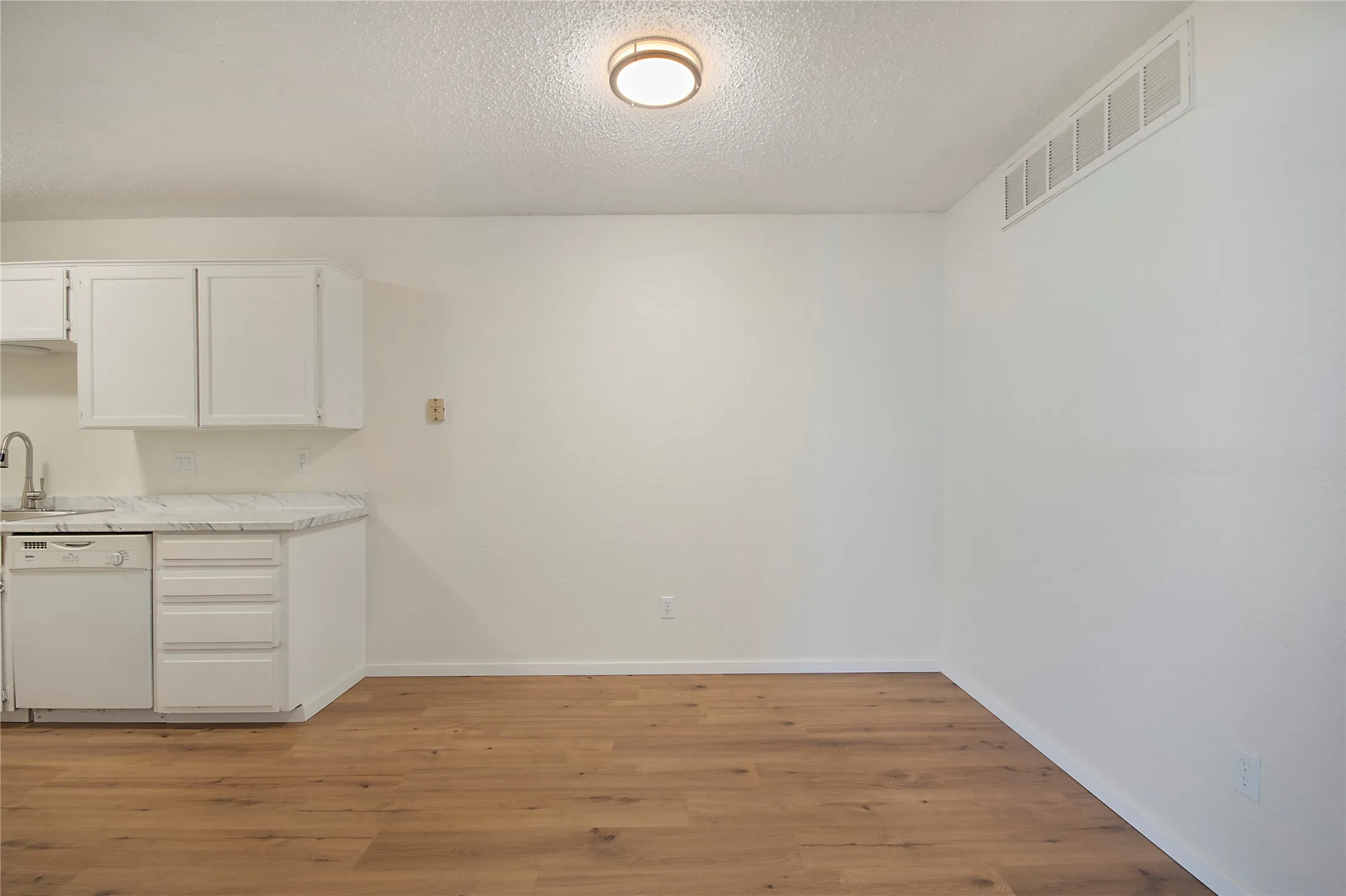Wood-finish flooring, white cabinetry, integrated dishwasher, gooseneck faucet, and light-colored countertops
