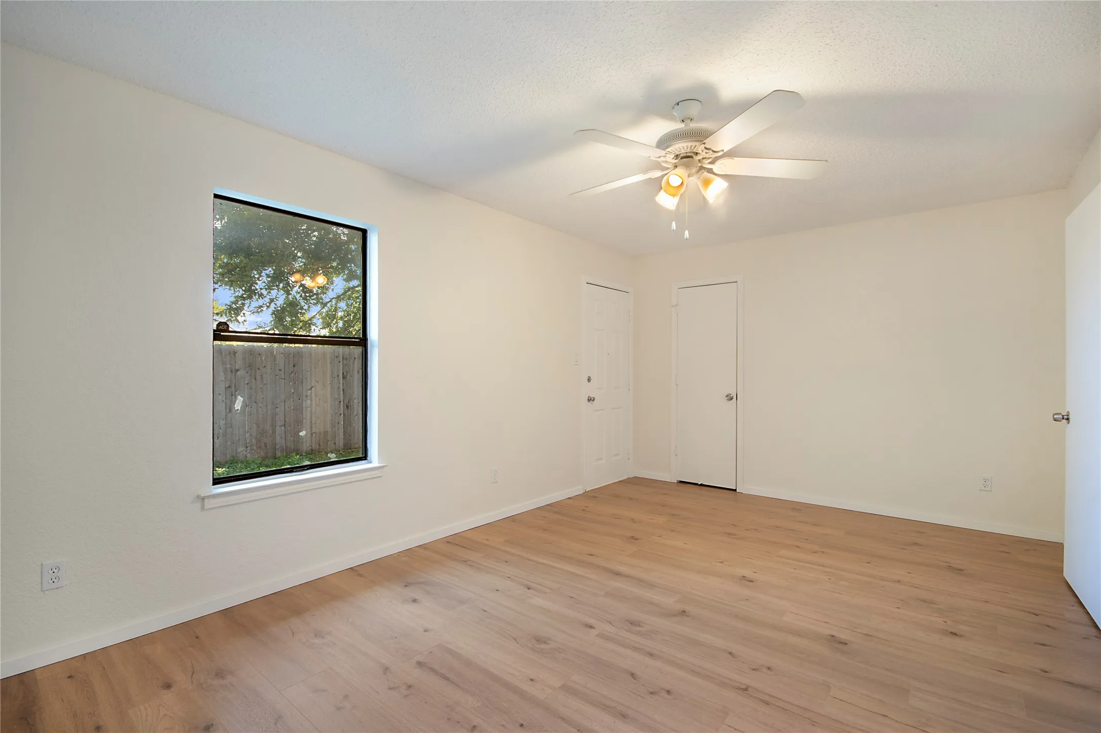 Wood-finish flooring, white walls, ceiling fan with light fixture, single window, and multiple doors