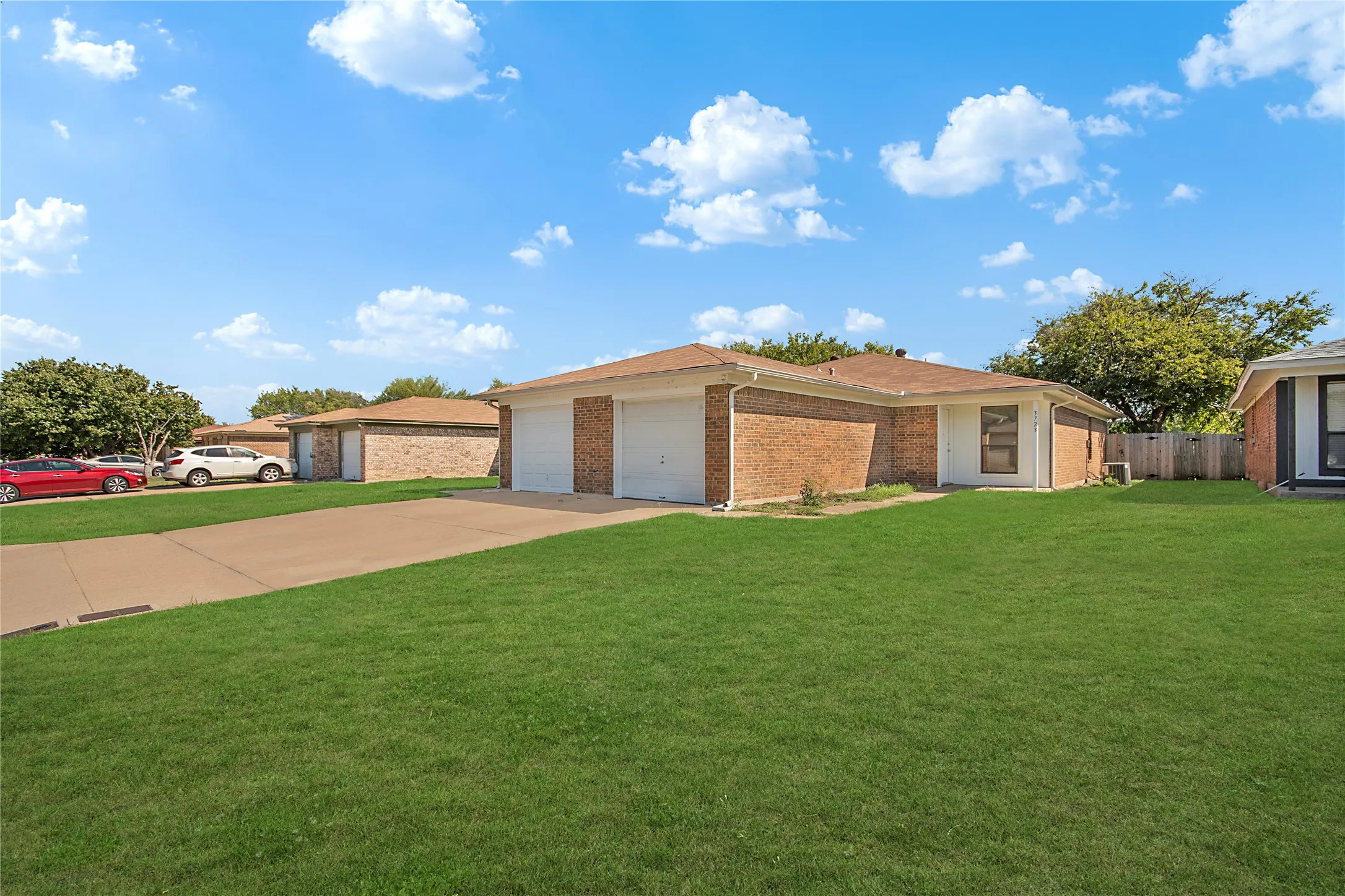 Brick exterior with a brown roof and white garage doors, featuring a concrete driveway and a green lawn