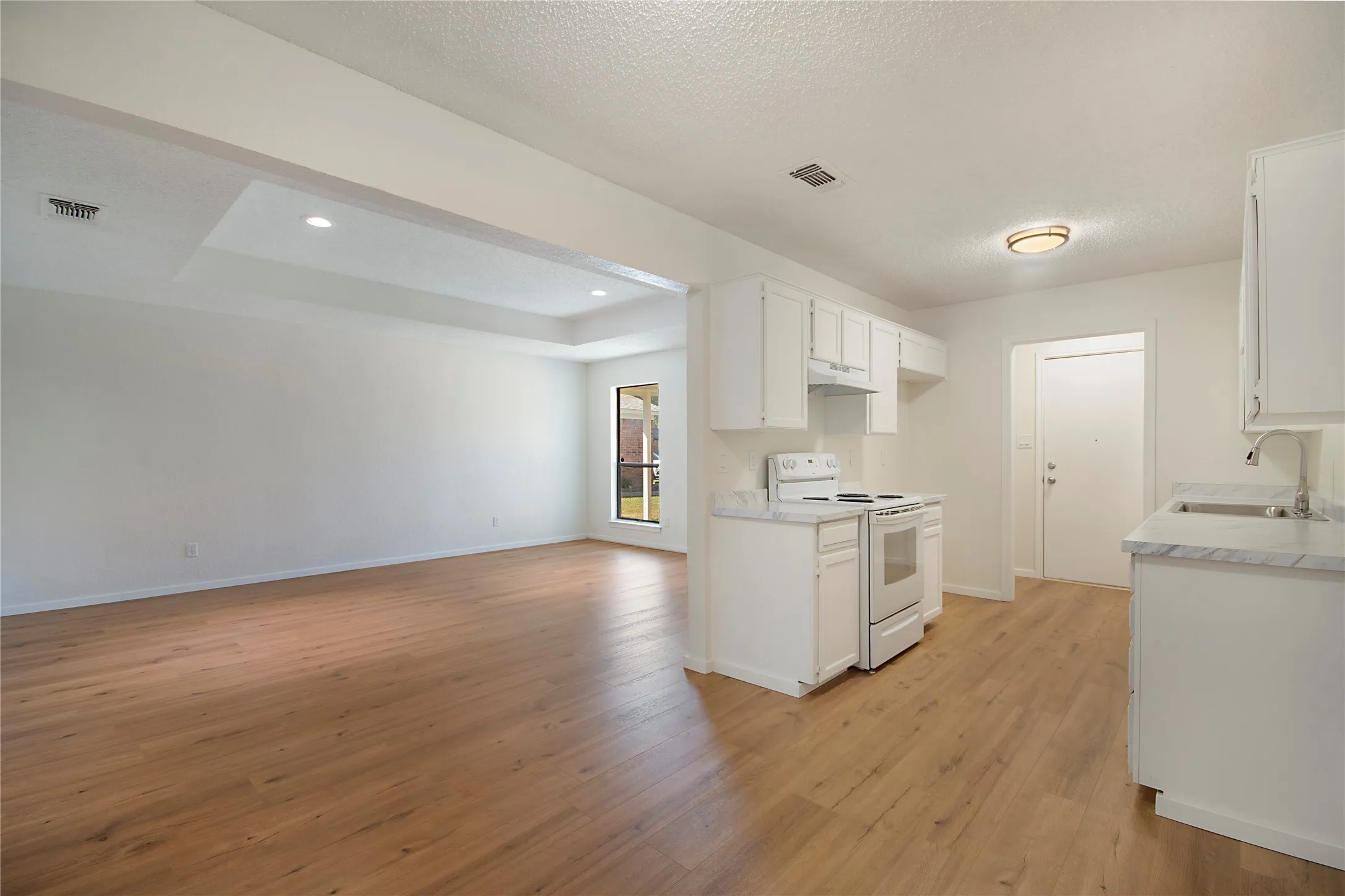 Wood-finish flooring throughout, white cabinetry, white electric range, and light-toned countertops