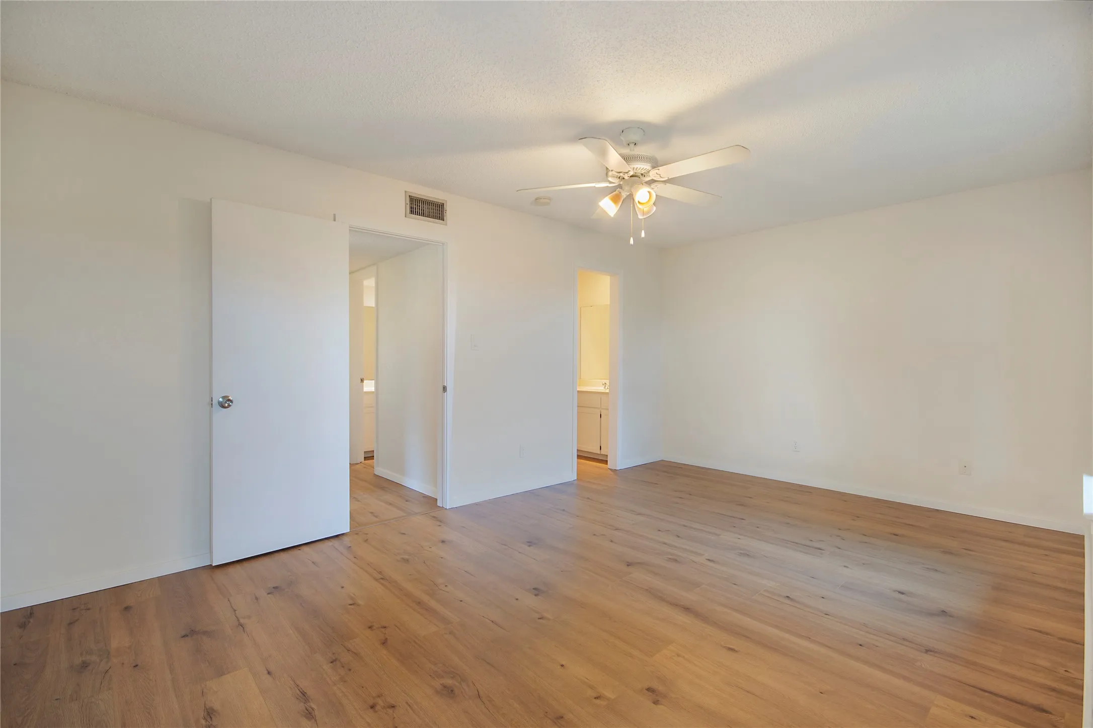 Spacious room featuring wood-finish flooring, a ceiling fan with integrated lighting, and neutral wall tones