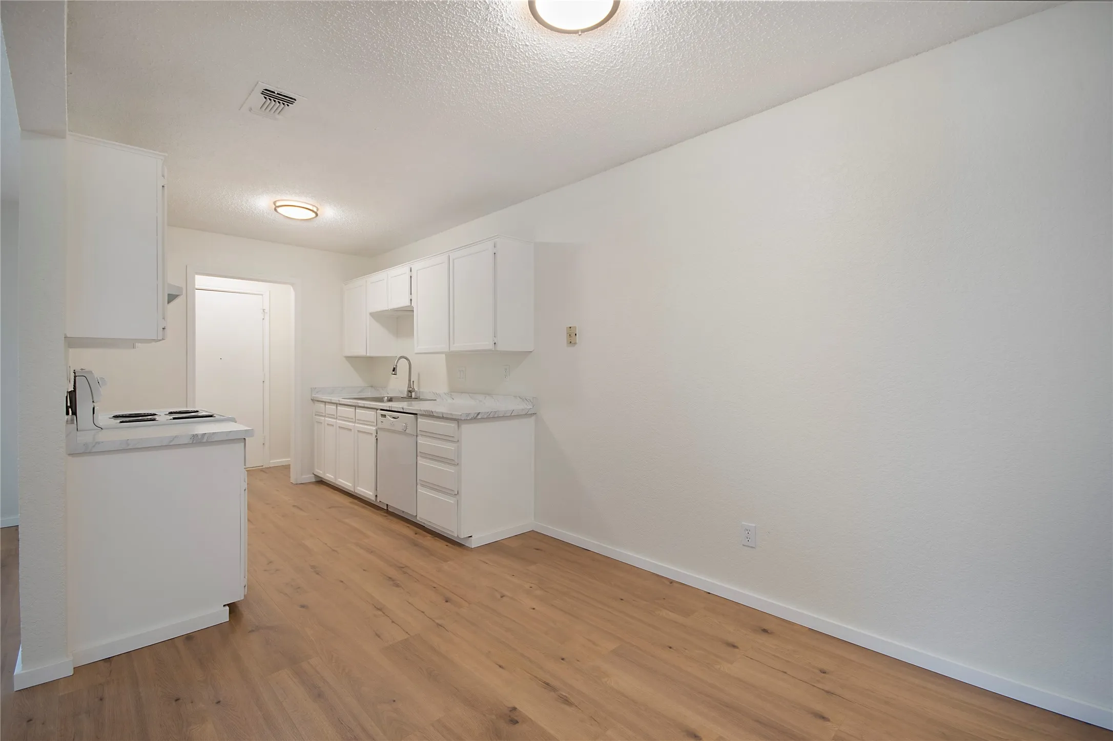 Kitchen featuring wood-finish flooring, white cabinetry, light-colored countertops, and a stainless steel sink