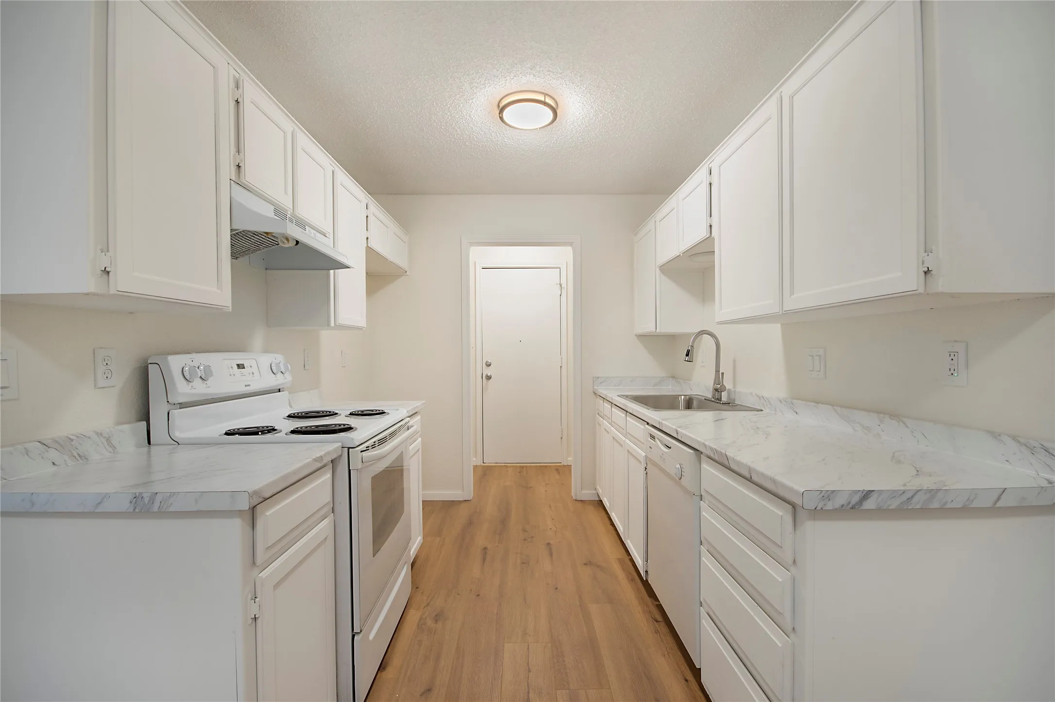 Galley kitchen featuring white cabinetry, wood-finish flooring, white appliances, and light-toned countertops