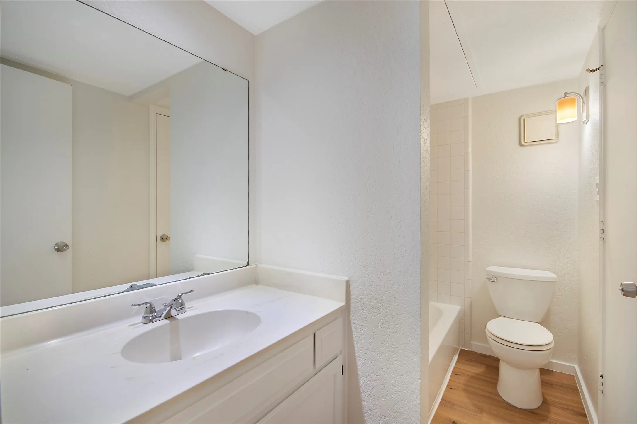 Single vanity with an integrated sink and chrome faucet, large mirror, and wood-finish flooring
