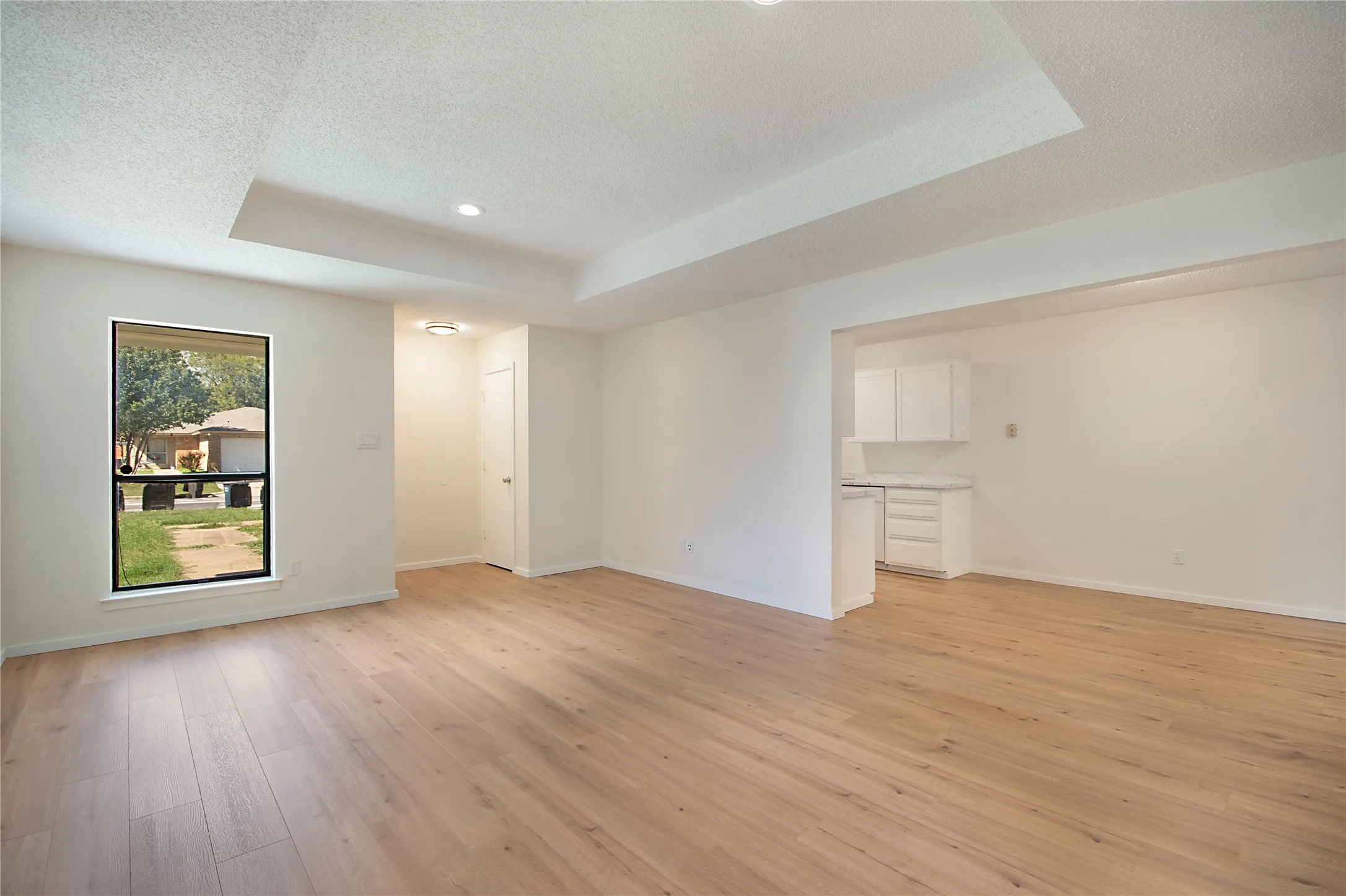 Recessed lighting, tray ceiling, wood-finish flooring, white cabinetry, and a window with a black frame