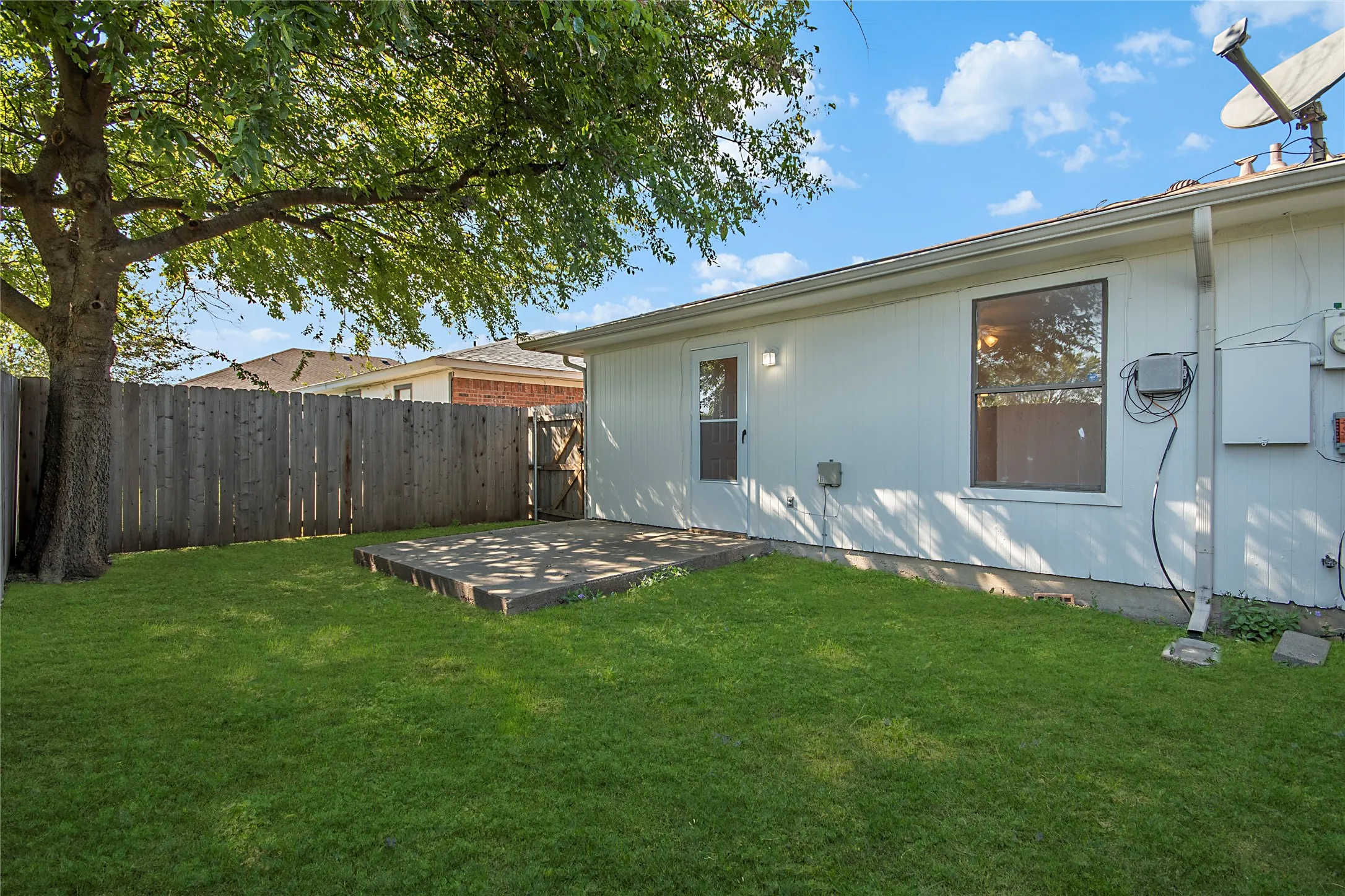 Expansive backyard featuring a manicured lawn, established tree, wood privacy fencing, and a concrete patio pad