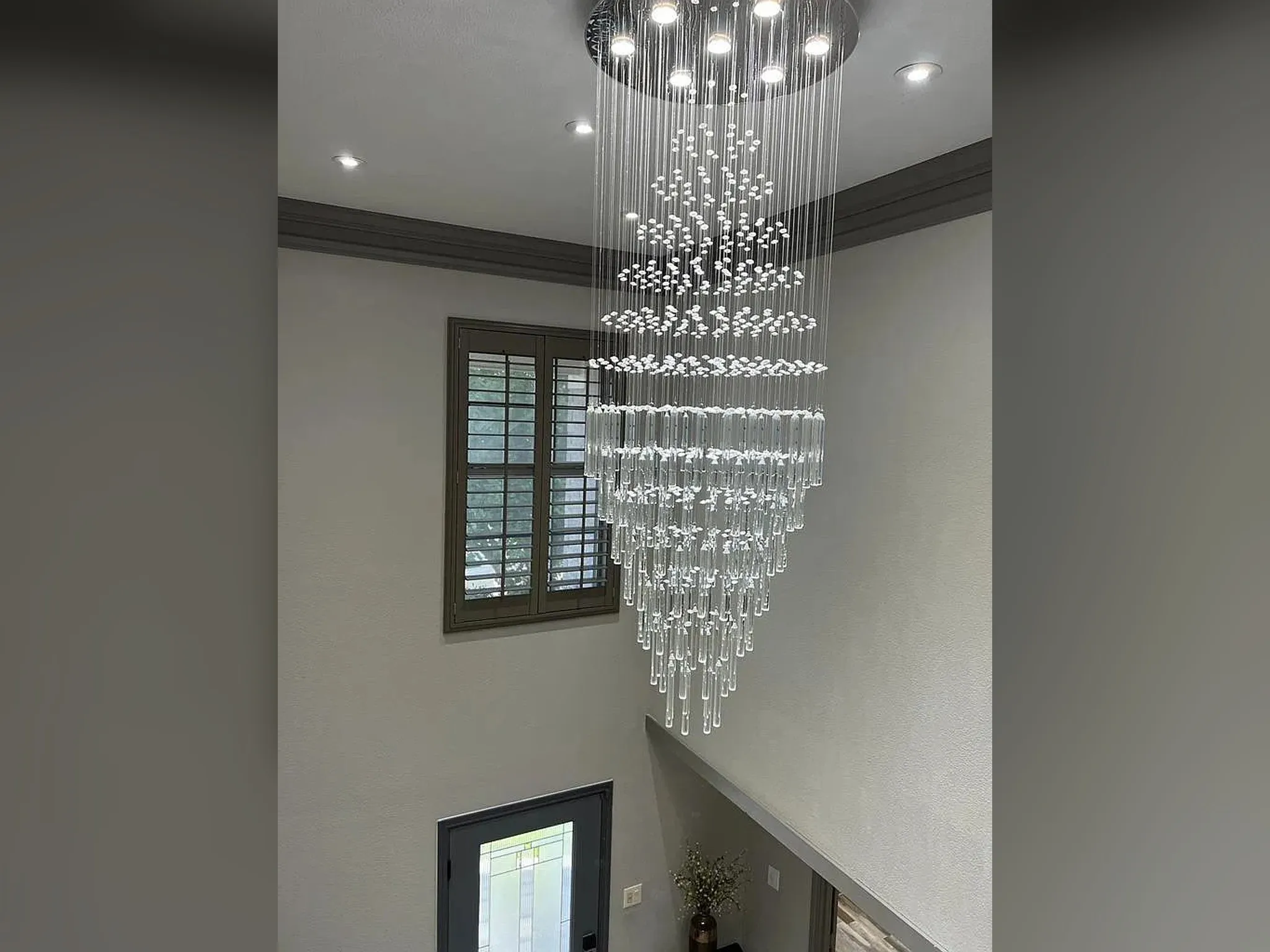 Multi-tiered chandelier with crystal accents, recessed ceiling lighting, and a window with plantation shutters