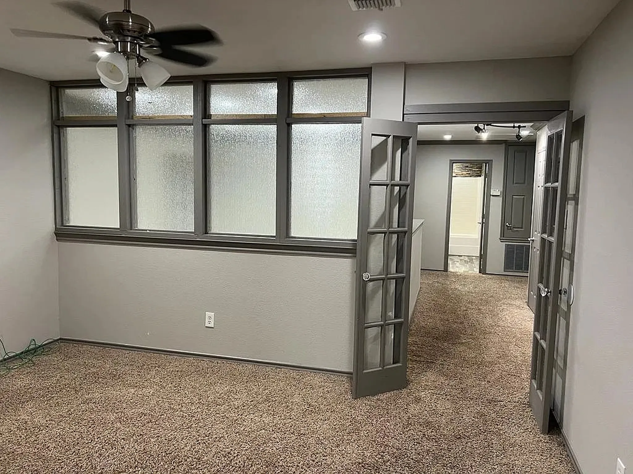 Carpeted interior with a ceiling fan, transom windows, and French doors leading to an additional space