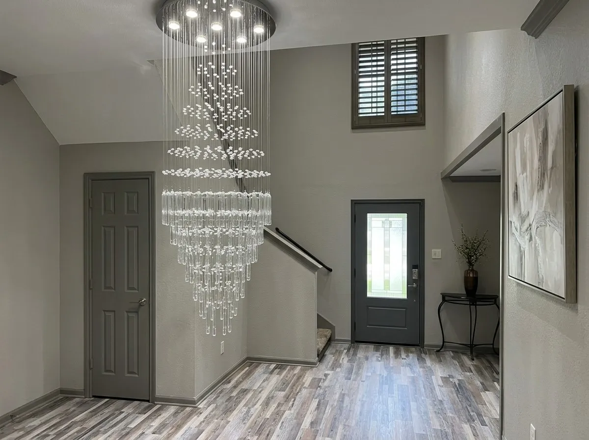 Two-story entryway featuring a multi-tiered crystal chandelier, wood-finish flooring, and a window with wood plantation shutters