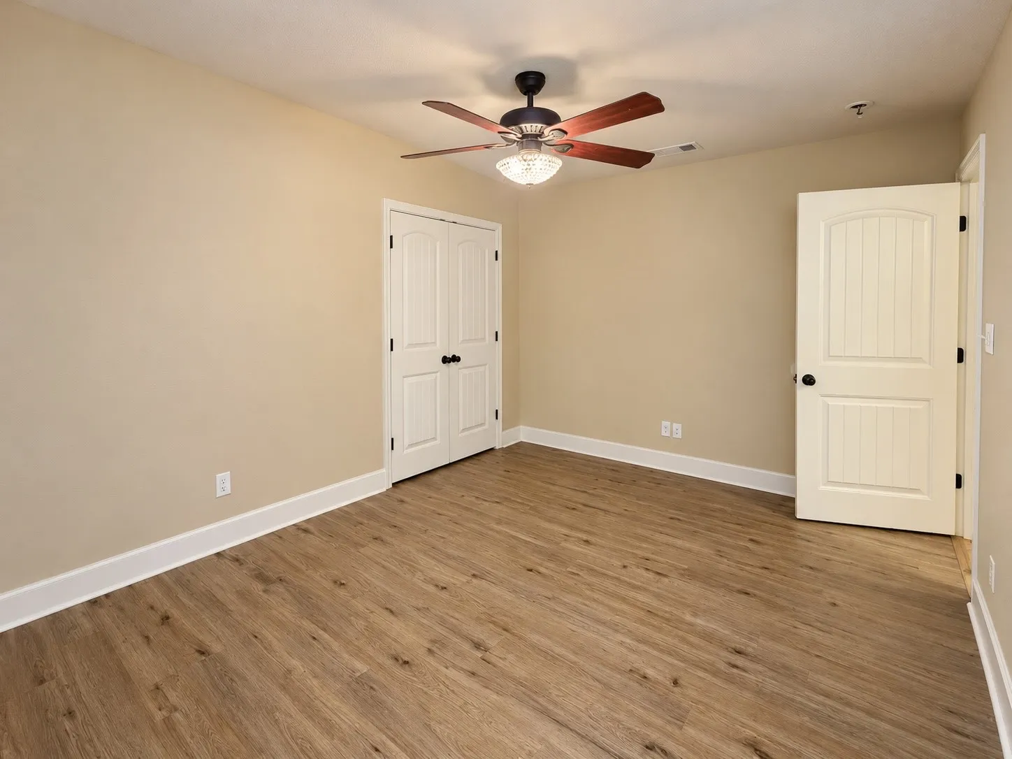 Wood-finish flooring, neutral wall tones, white trim, ceiling fan with integrated lighting, and white paneled doors with dark hardware