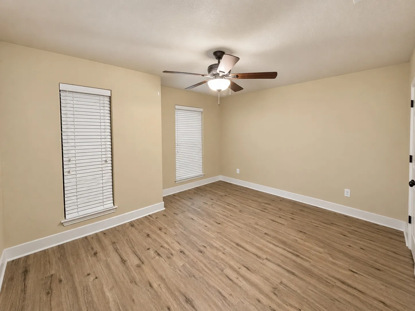Wood-finish flooring with white trim, two windows with blinds, and a ceiling fan with light fixture