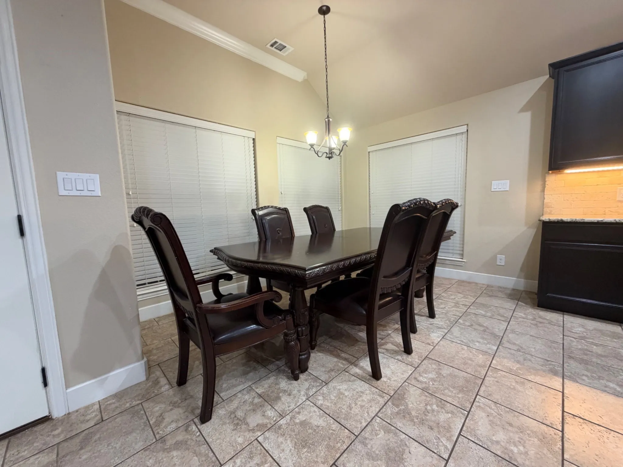 Vaulted ceiling with a chandelier, tile flooring, window with blinds, and built-in cabinetry with a stone countertop