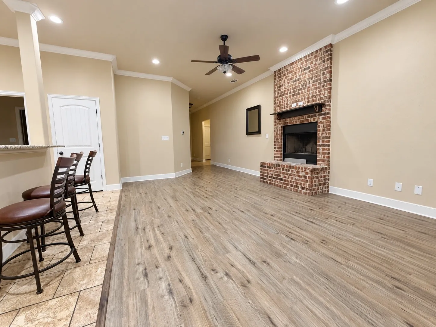 Open-concept living space featuring wood-finish flooring, a brick-surround fireplace with a mantel, and recessed lighting
