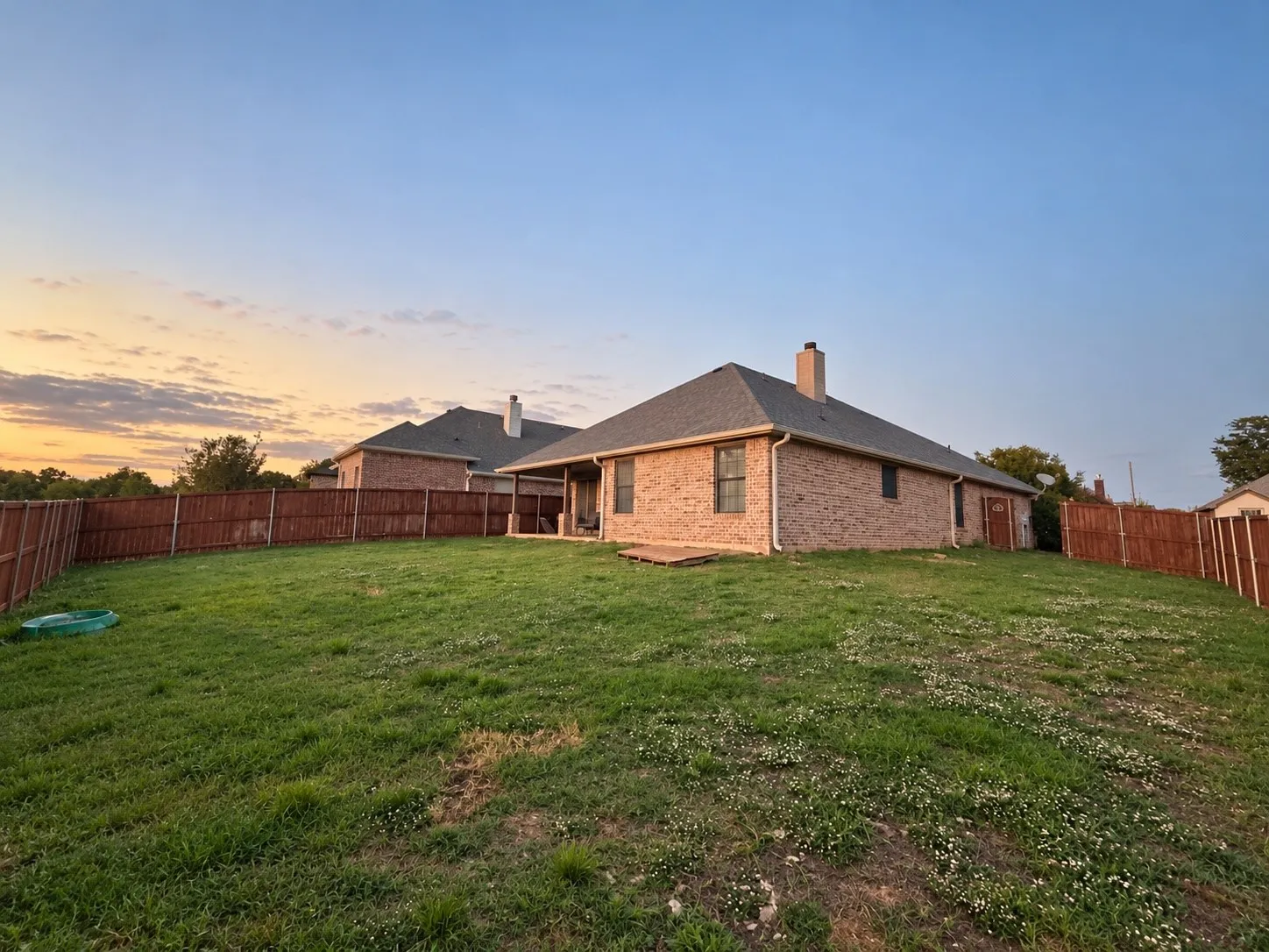 Expansive backyard featuring a manicured lawn, full privacy fencing, and a brick-clad exterior