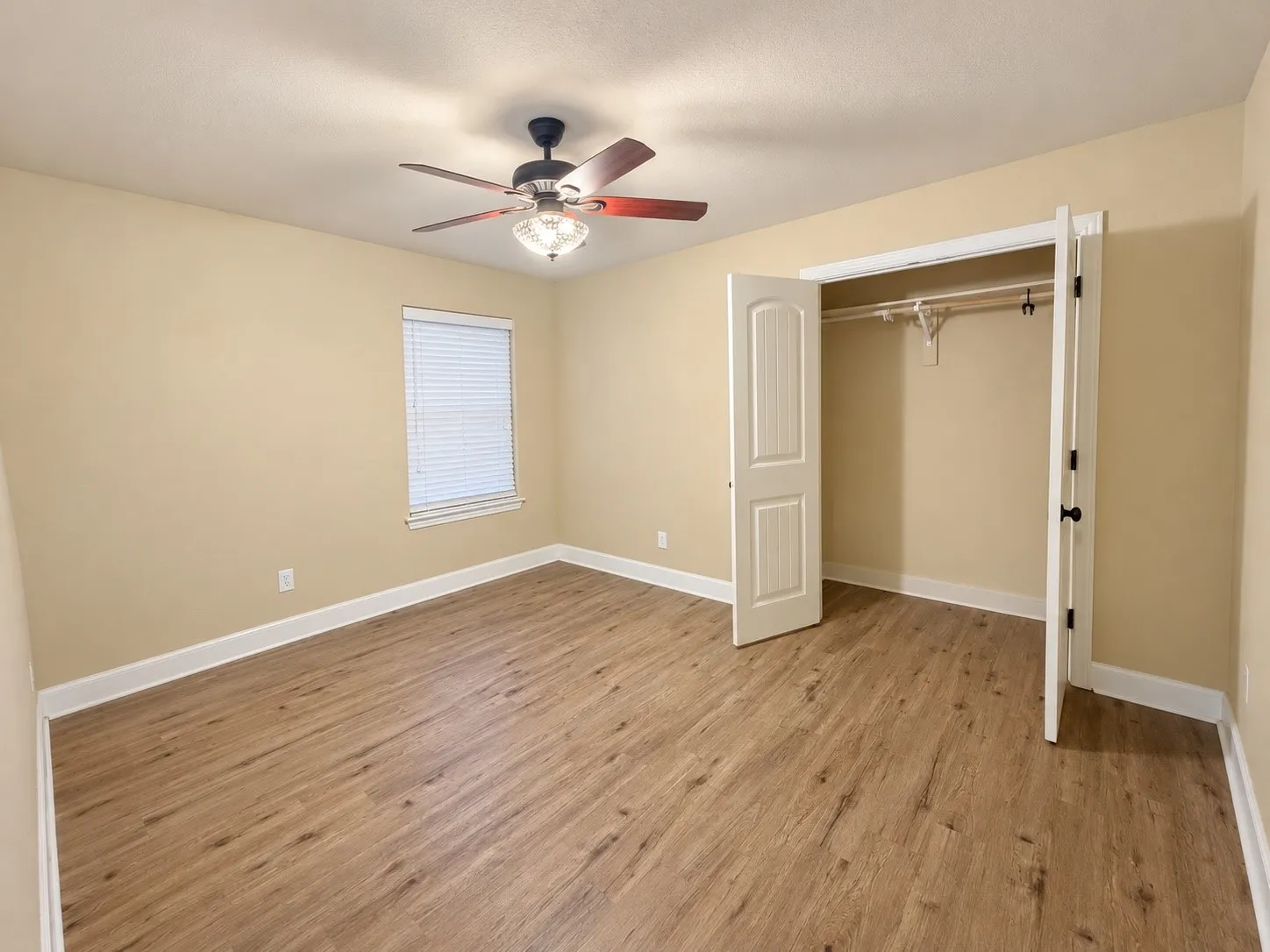 Wood-finish flooring, ceiling fan, window with blinds, and a closet with bifold doors