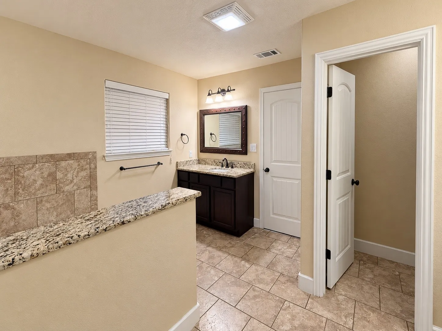 Tile flooring, half-wall with granite countertop, vanity with dark wood-finish cabinetry, granite countertop, and integrated sink