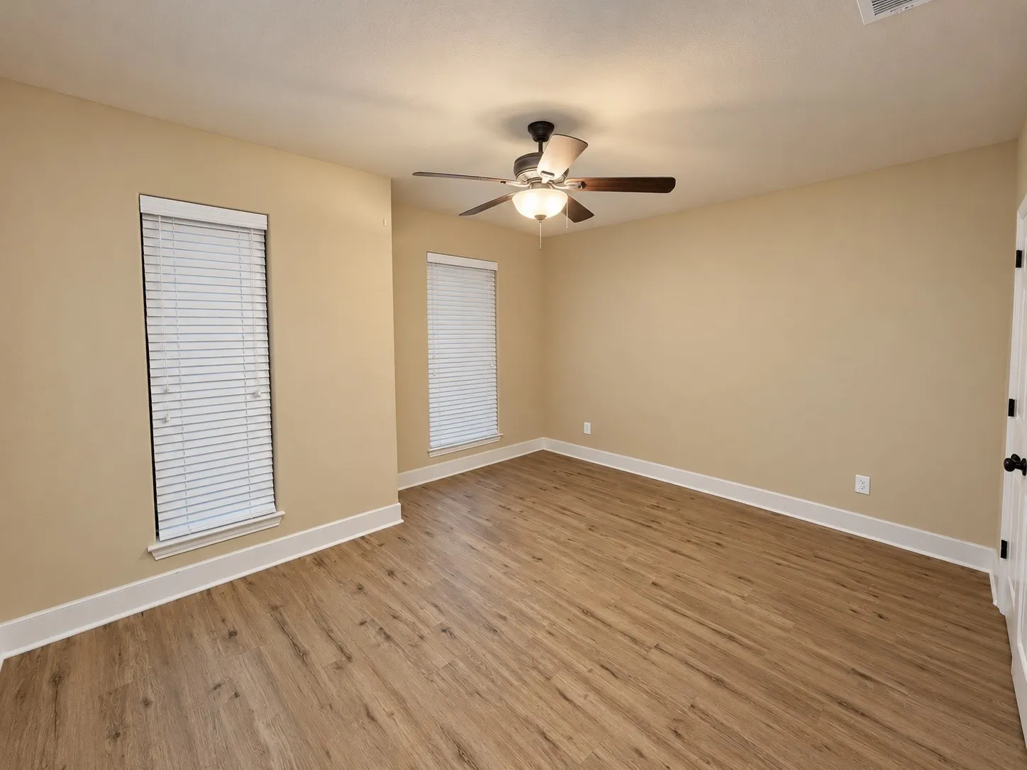 Wood-finish flooring, neutral wall tones, two windows with white blinds, white trim, and a ceiling fan with integrated lighting