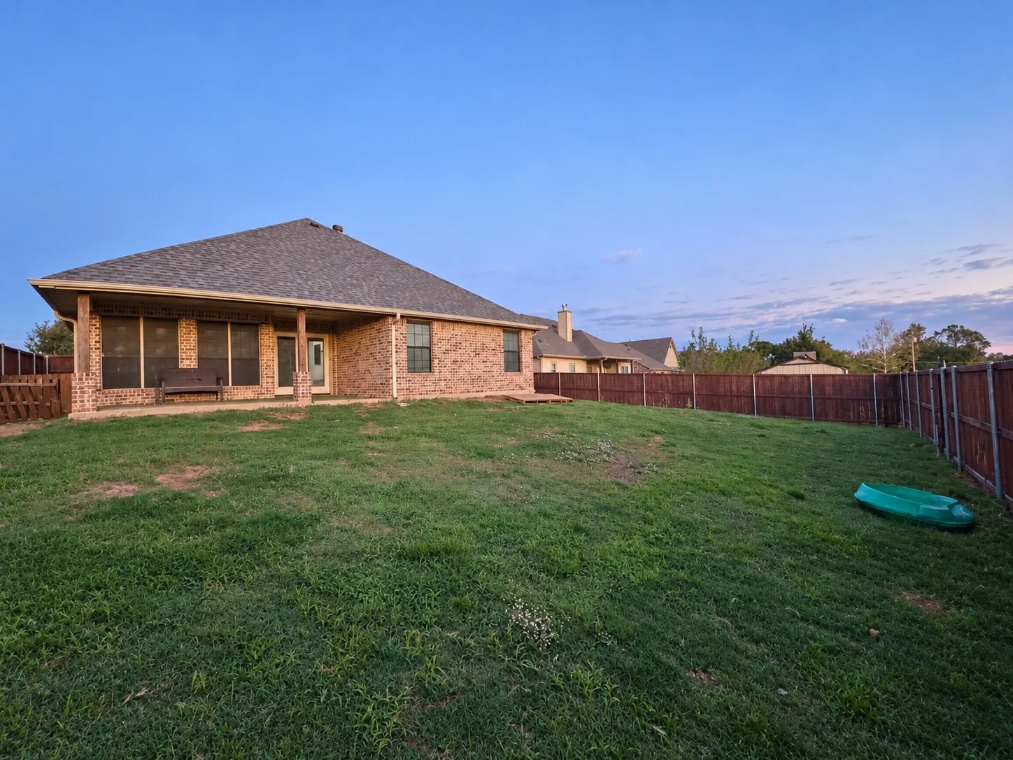 Brick exterior with a covered patio, fenced backyard, and a shingled roof