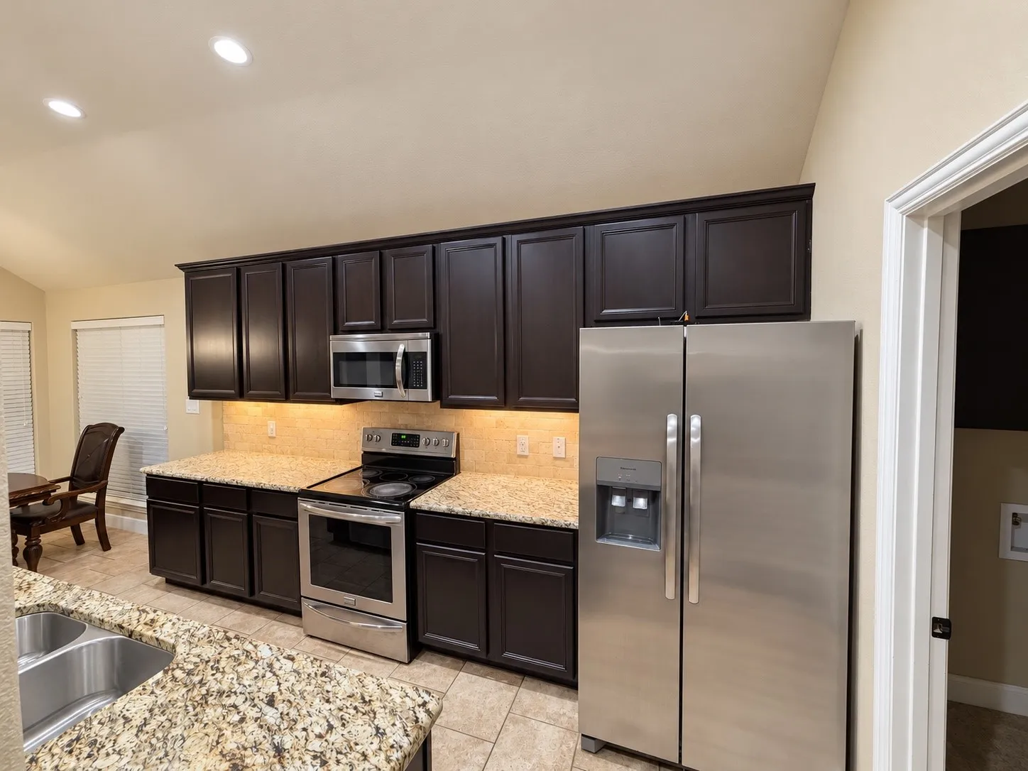 Kitchen featuring dark wood cabinetry, light granite countertops, stainless steel appliances, and recessed lighting