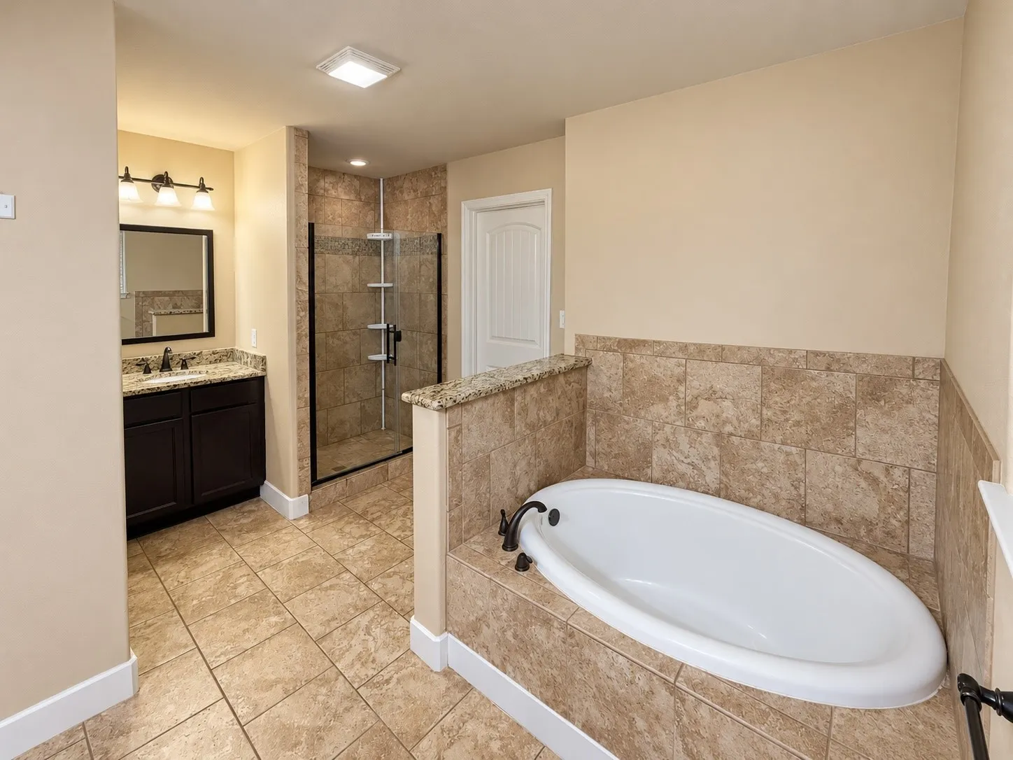 Bathroom featuring a tiled soaking tub, a separate glass-enclosed shower with tiled walls, a vanity with a stone countertop, and tiled flooring throughout