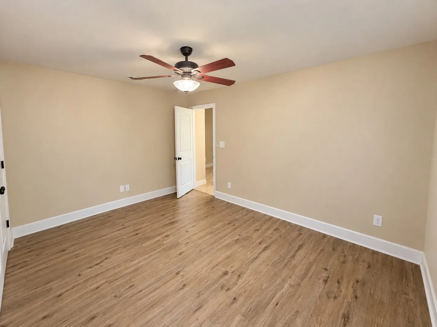 Wood-finish flooring, neutral wall paint, ceiling fan with integrated lighting, and white trim