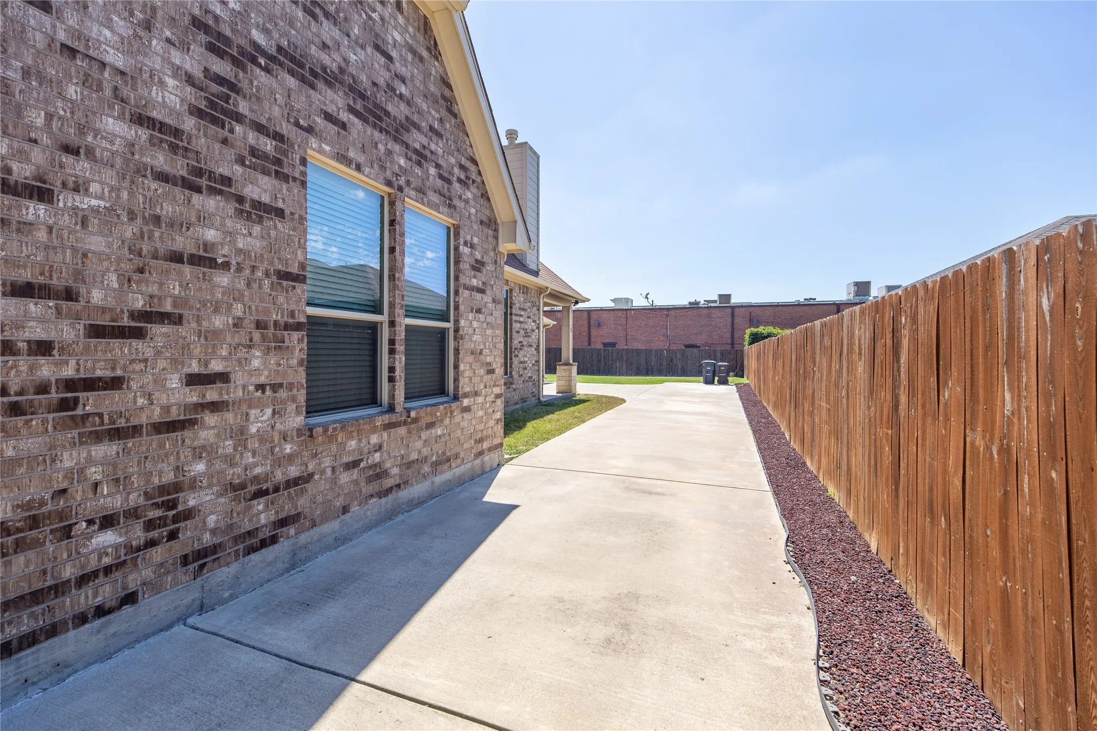 Brick exterior facade with multiple windows, concrete walkway, and a privacy fence