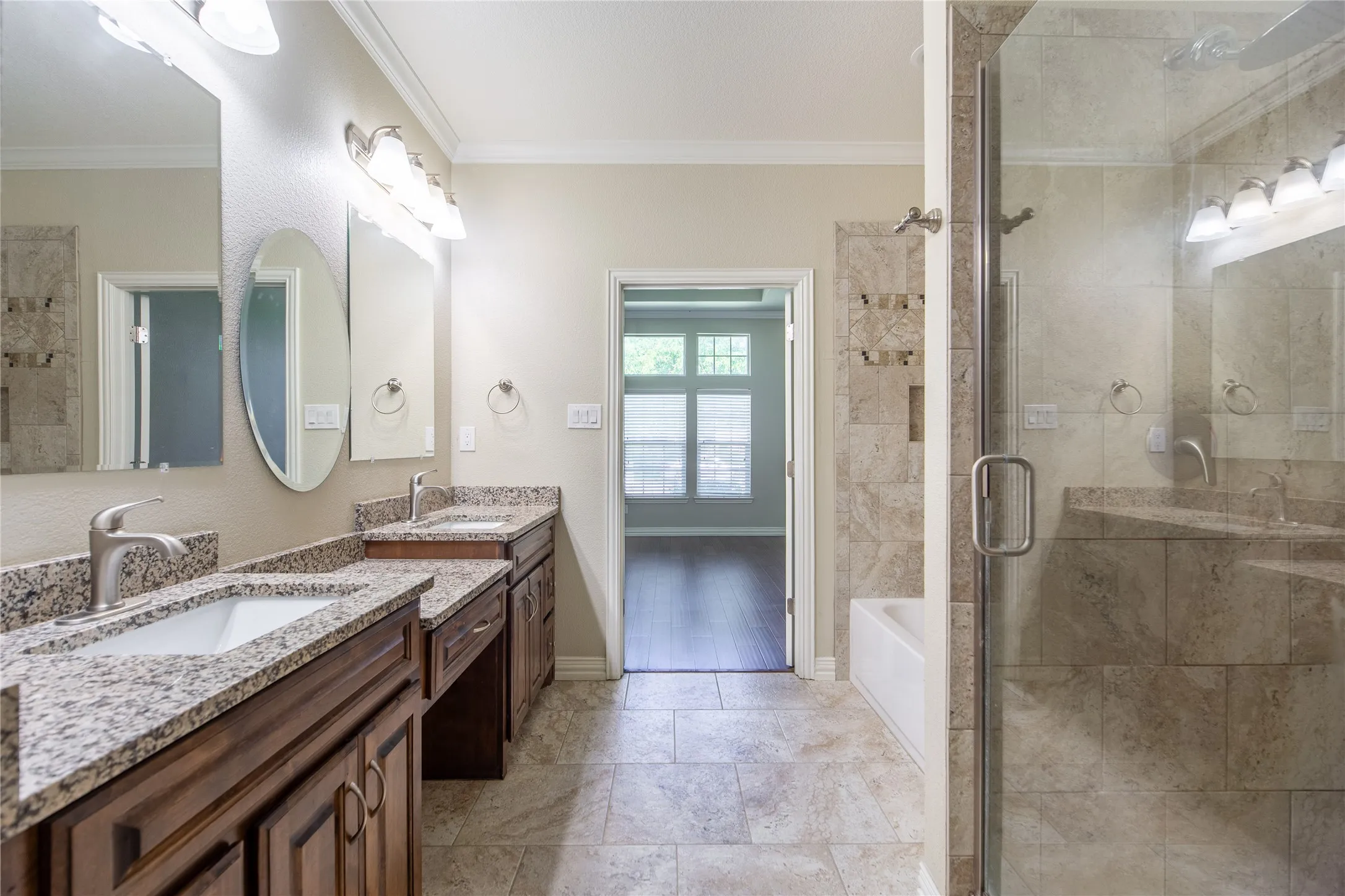 Luxurious primary bathroom suite featuring dual vanities with granite countertops, wood-finish cabinetry, and polished nickel fixtures