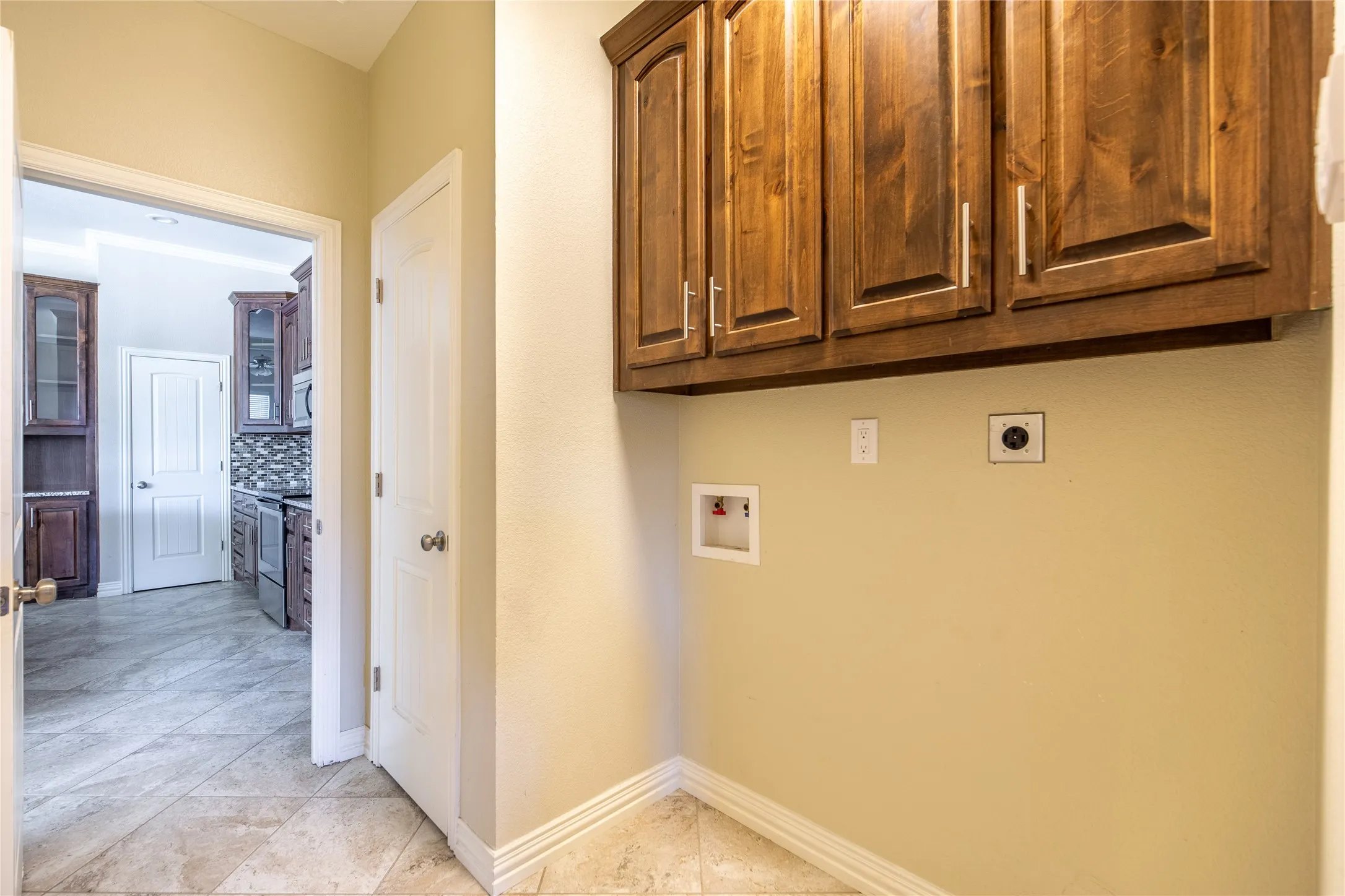 Laundry area with wood-finish cabinetry and tile flooring